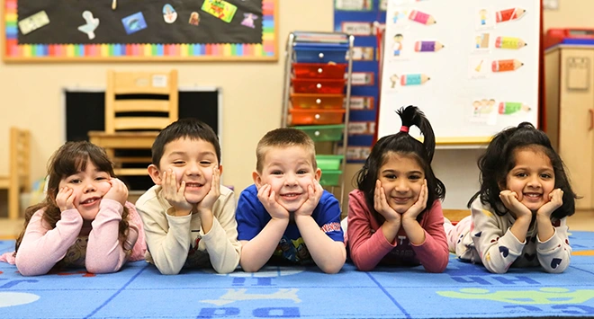 Little children lying on the floor resting heads on hands and smiling at the camera