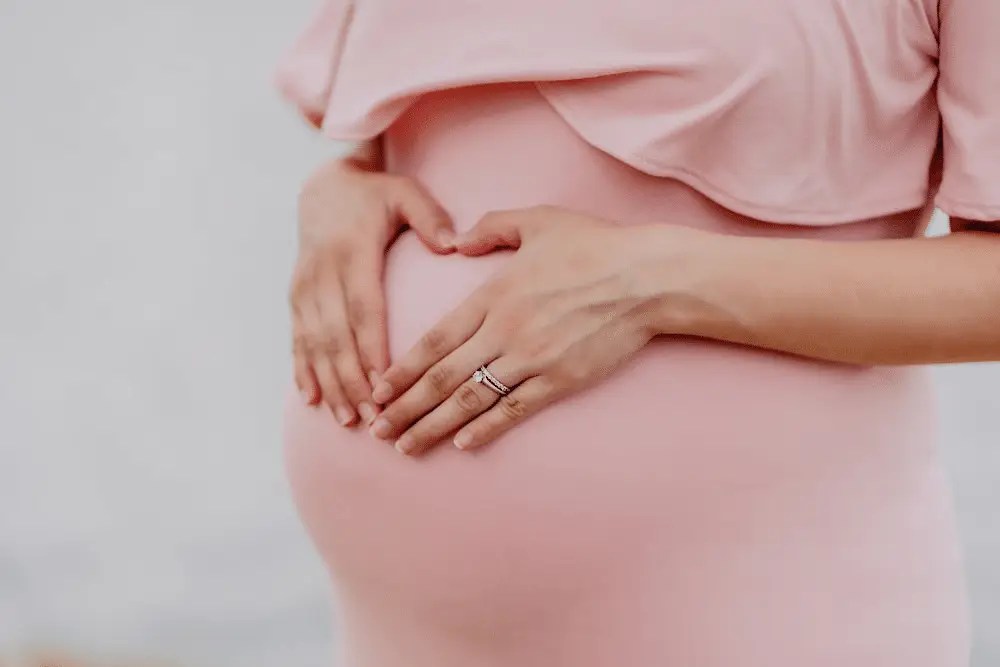 Close-up of a pregnant woman in a pink dress lovingly cradling her belly, symbolizing prenatal care and wellness.