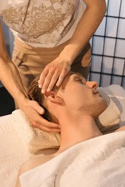 man lying down covered with a towel getting a neck massage