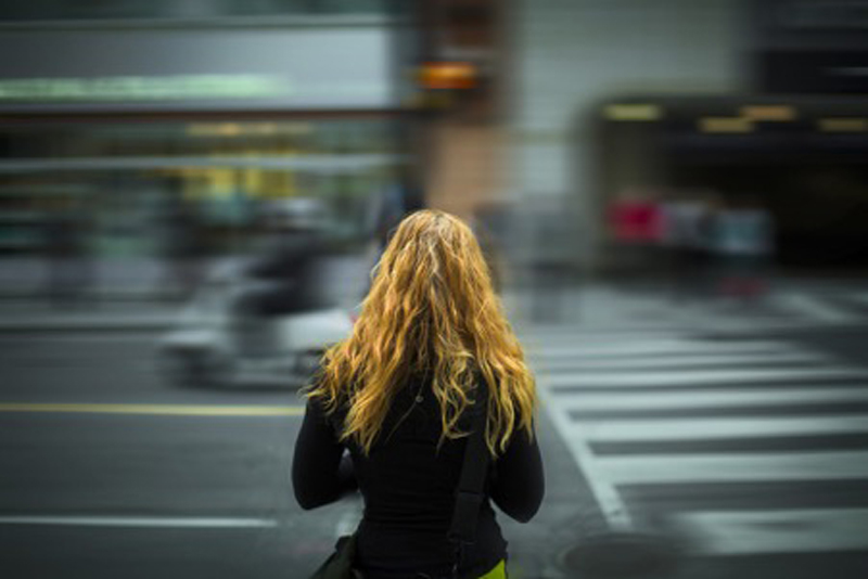 A blonde haired woman stands in front of a busy street