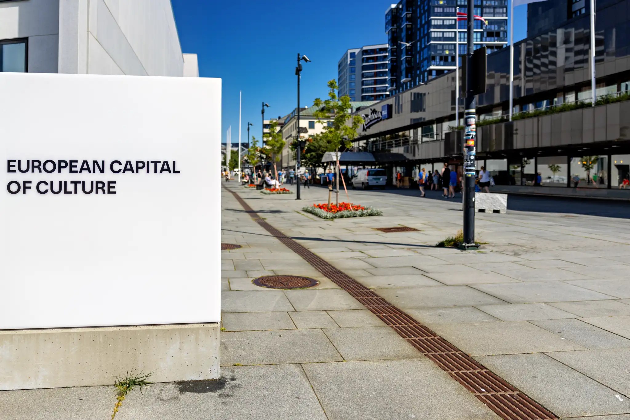 Straßenszene mit moderner Architektur und einem weißen Schild mit der Aufschrift 'European Capital of Culture'