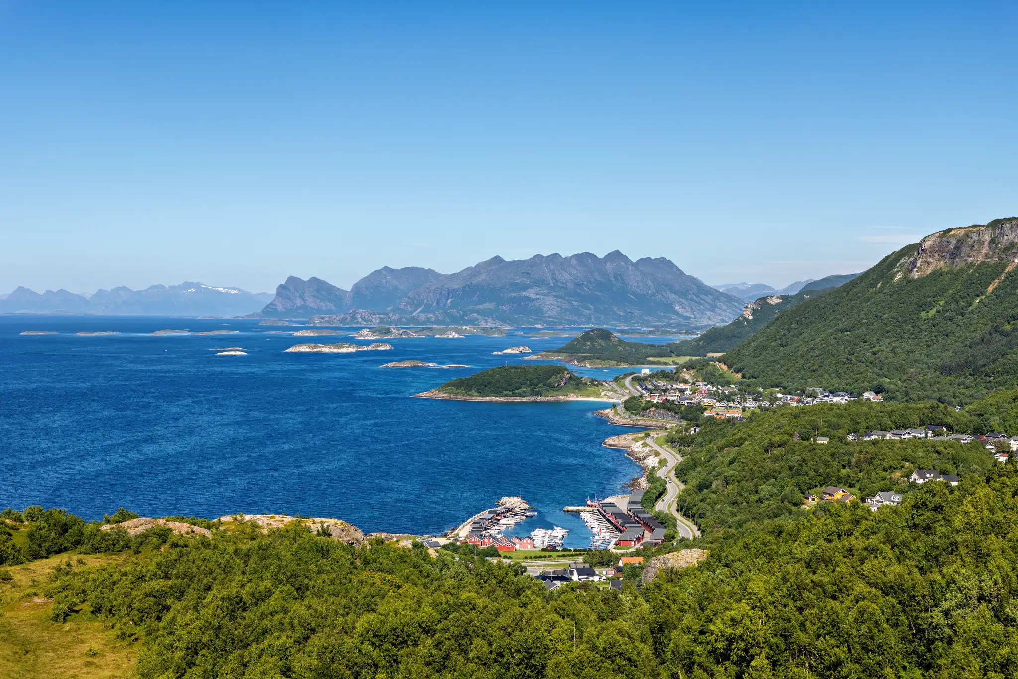 Blick auf die Küste von Bodø mit blauem Meer, kleinen Inseln, Hafen und Bergen im Hintergrund bei klarem Himmel