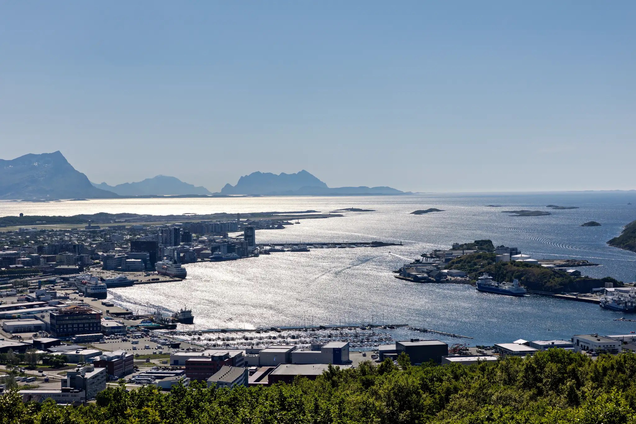 Blick auf eine Küstenstadt mit Hafen und Inseln im Meer, Berge im Hintergrund unter klarem Himmel