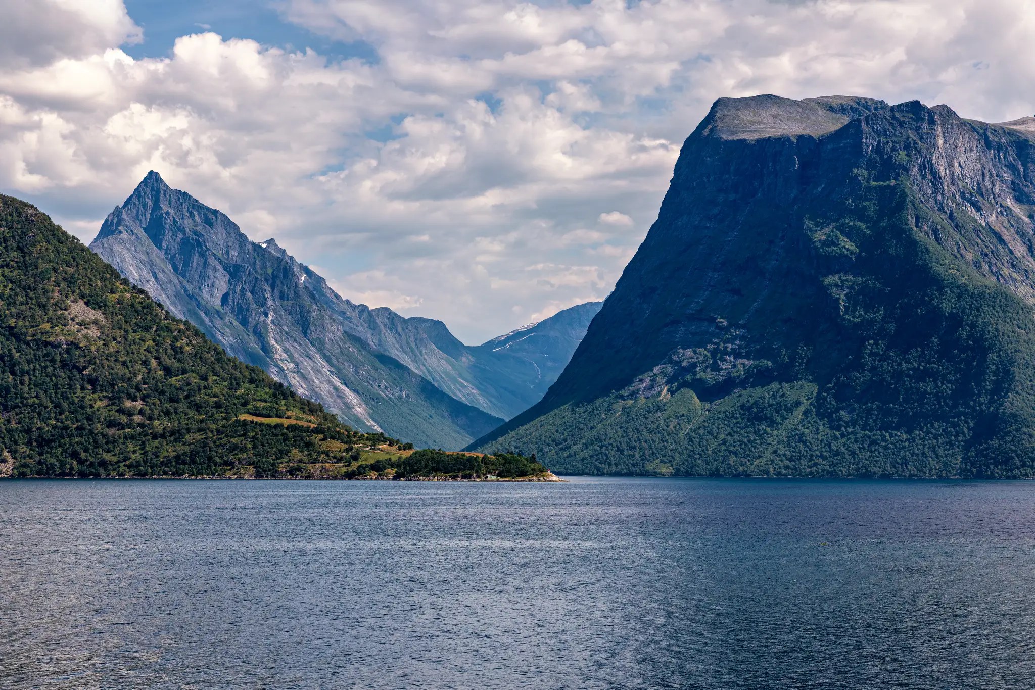 Hjørundfjorden mit steilen bewaldeten Bergen und ruhigem Wasser unter bewölktem Himmel