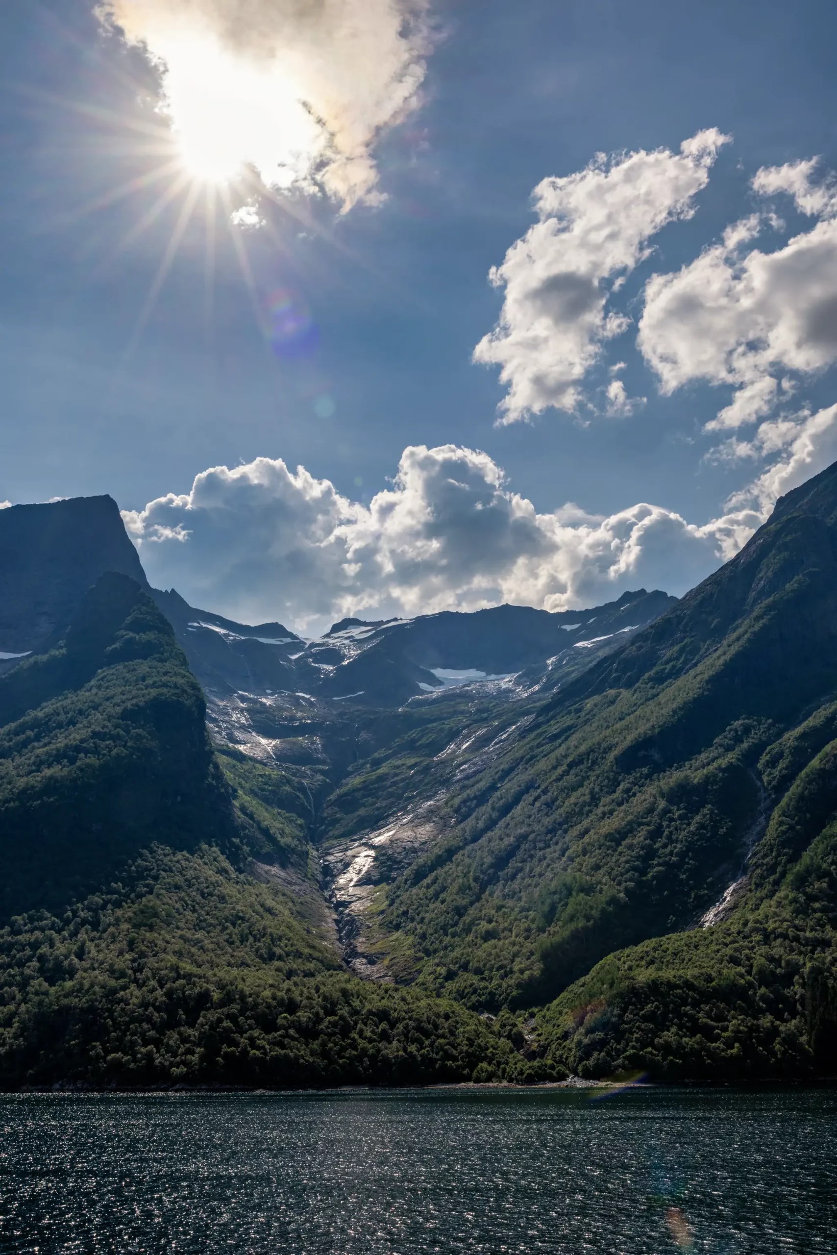 Sonniger Himmel über bewaldeten Bergen und Wasser im Hjørundfjord, Norwegen