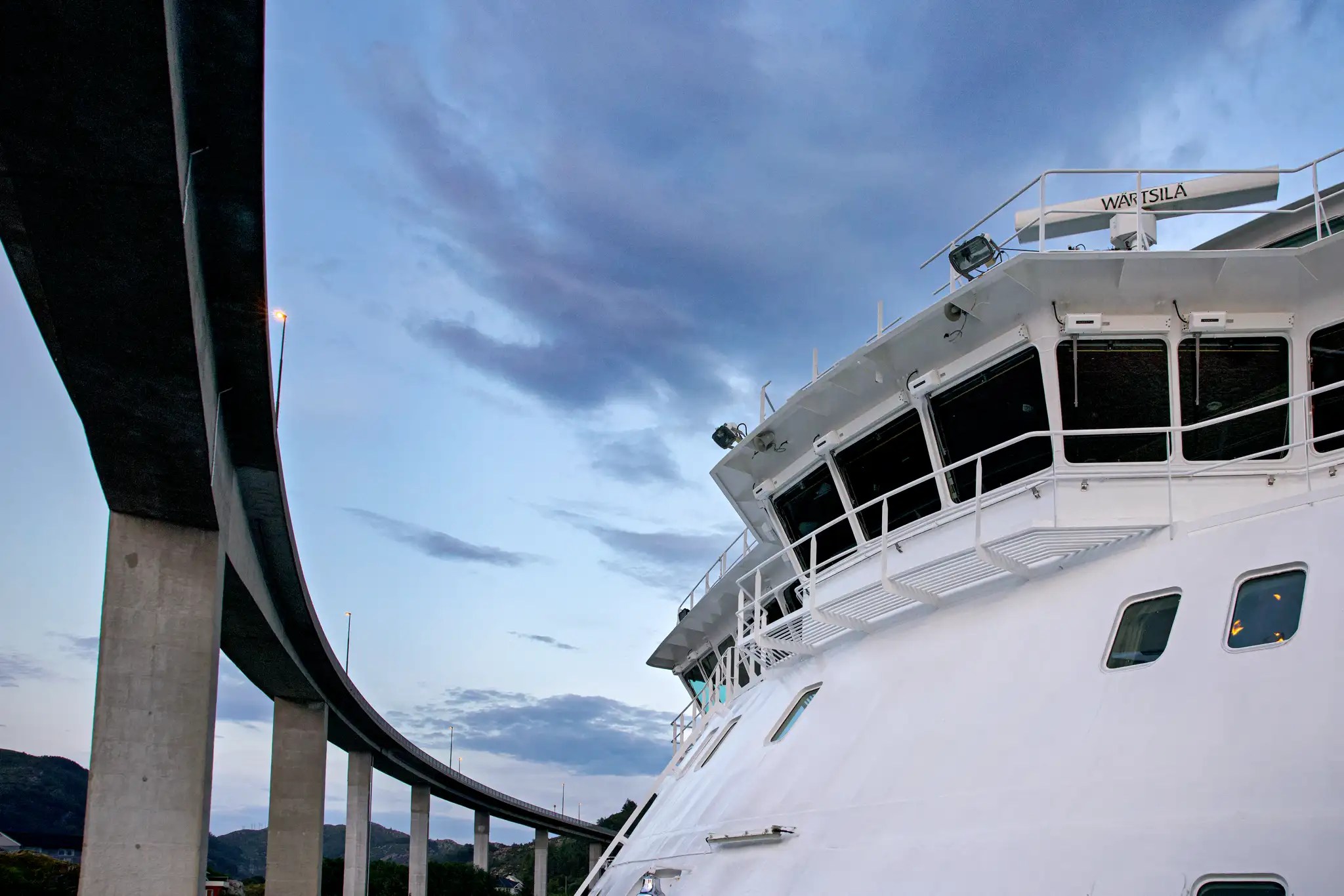 Brücke eines Hurtigruten-Schiffs unter einer Brücke bei Abenddämmerung