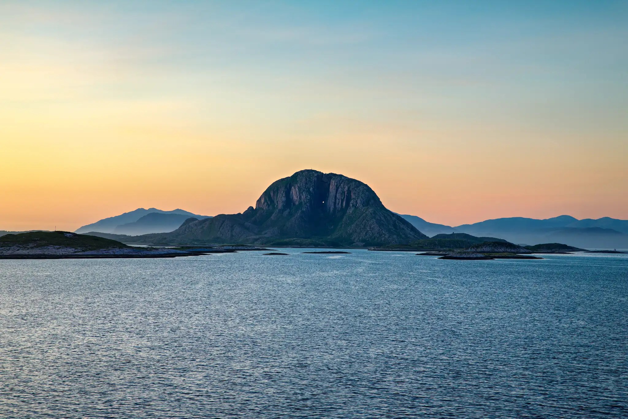 Felseninsel mit markantem Berg vor ruhigem Meer bei Sonnenuntergang