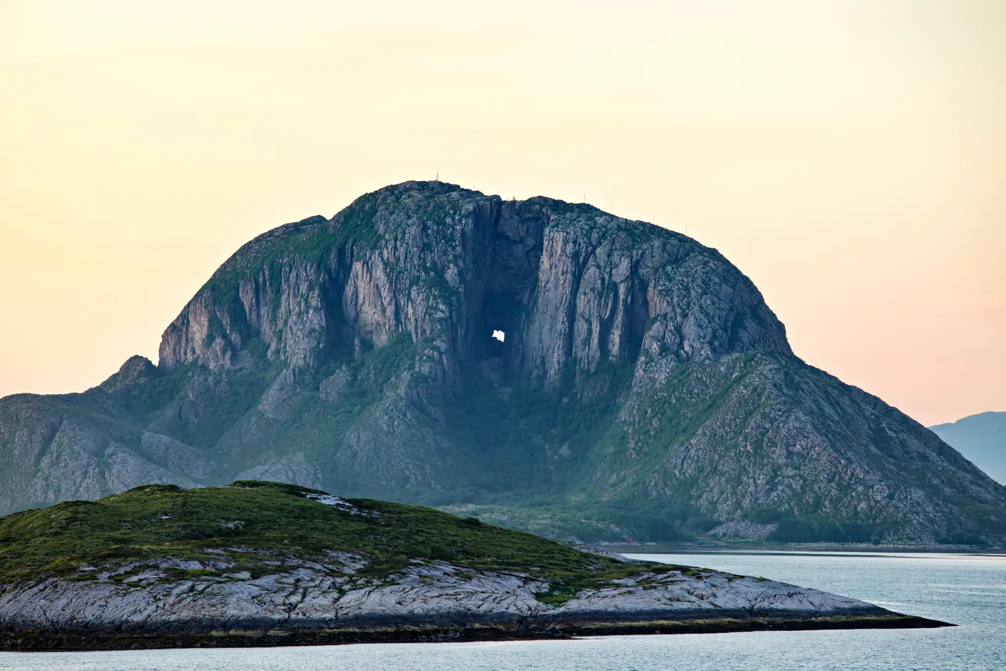 Großer Berg mit natürlichem Felsfenster über ruhigem Meer bei Sonnenuntergang
