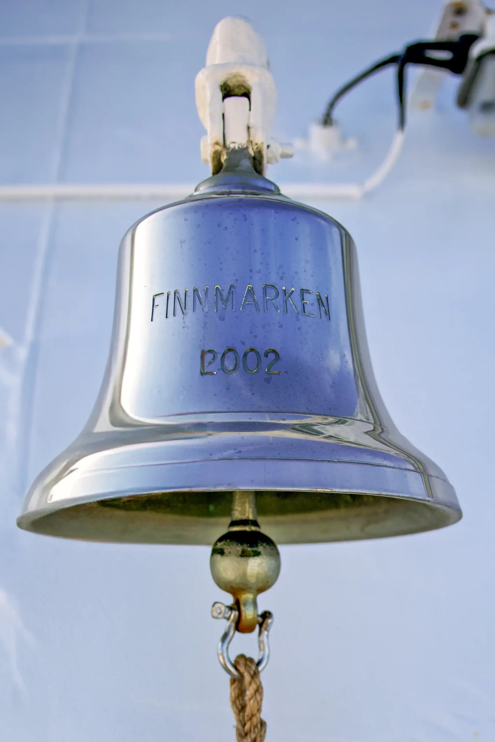 Schiffsglocke mit der Gravur 'FINNMARKEN 2002', aufgehängt an einer weißen Halterung