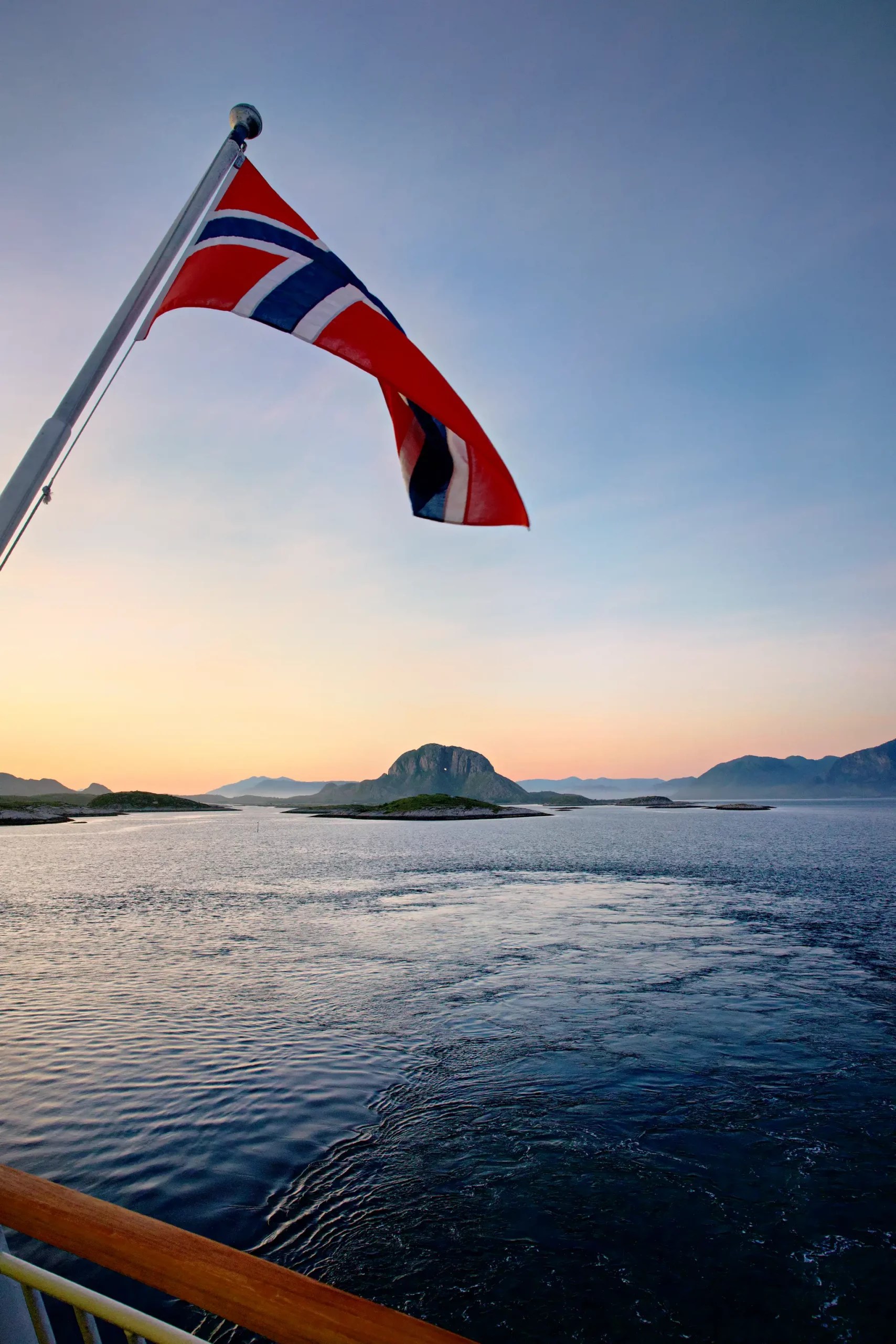 Norwegische Flagge weht auf einem Schiff mit Blick auf ruhige See und Inseln bei Sonnenuntergang