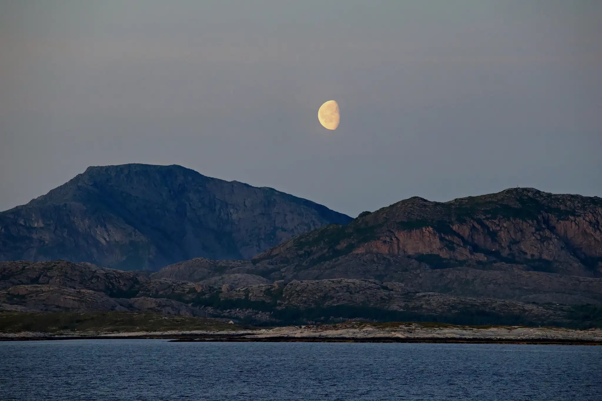 Halbmond über zerklüfteten Bergen am Meer bei Dämmerung