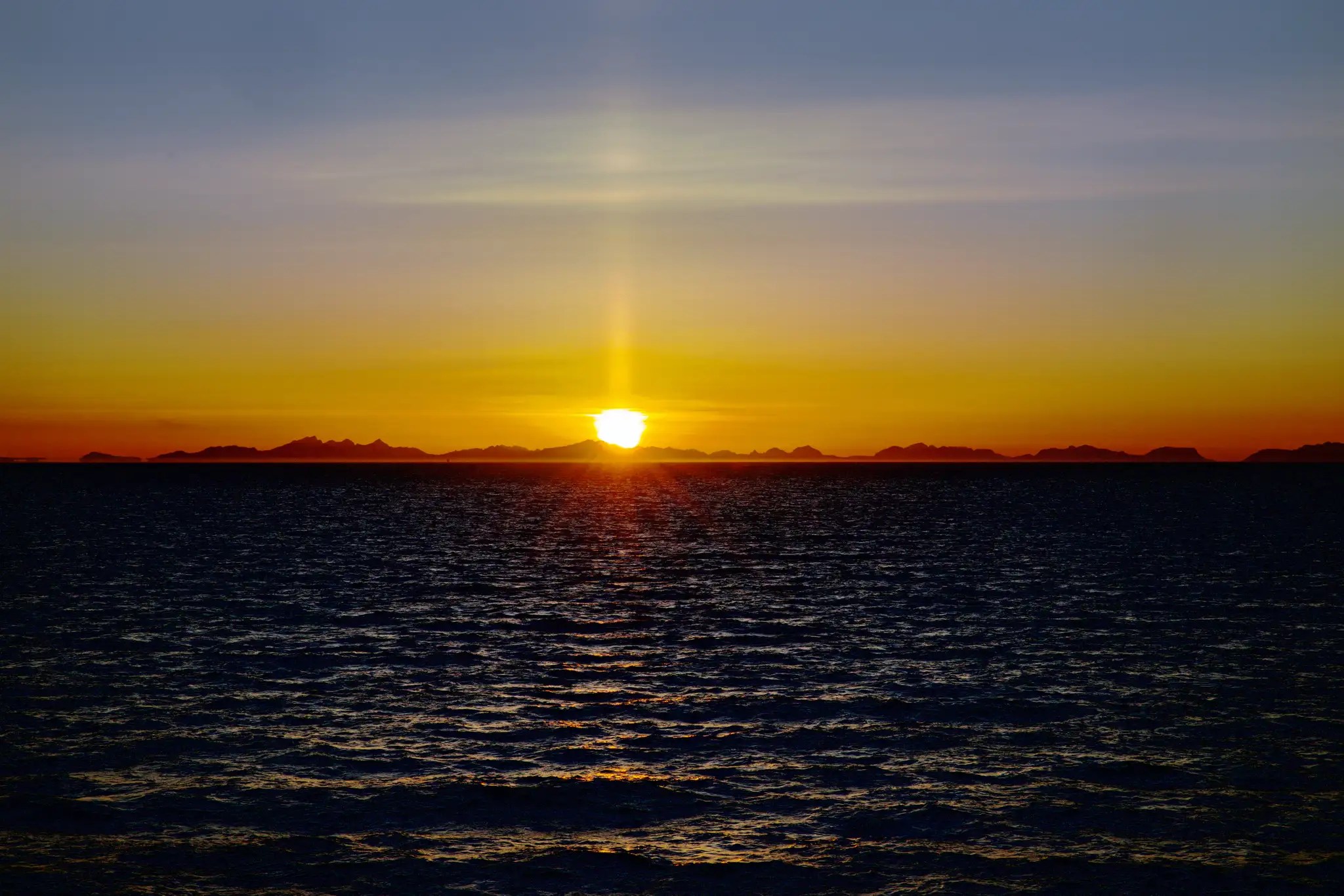 Sonnenuntergang über dem Meer mit dunklen Bergen am Horizont