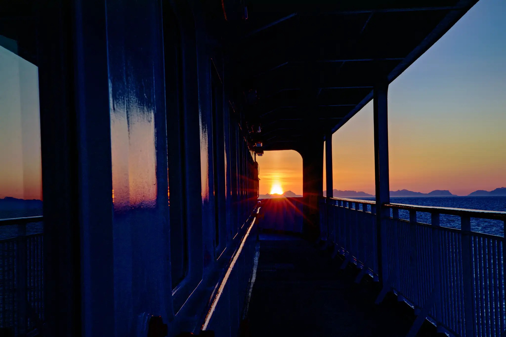 Sonnenuntergang über dem Meer gesehen vom Deck eines Schiffes mit Geländer und Fensterwand