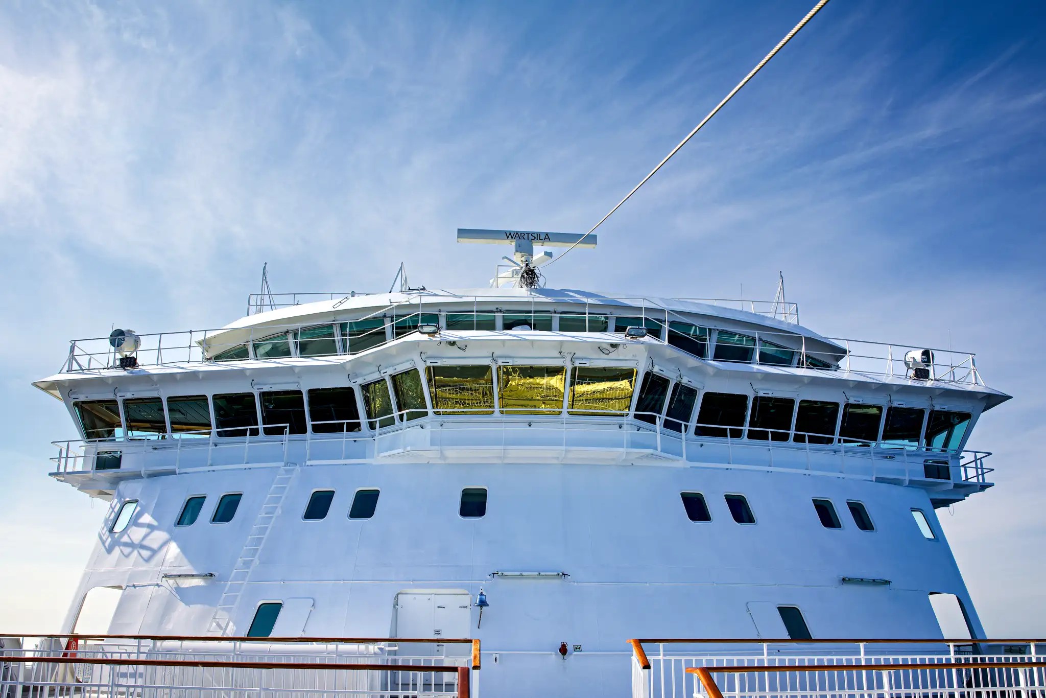 Vorderansicht eines weißen Kreuzfahrtschiffs mit Brücke und Antennen unter blauem Himmel