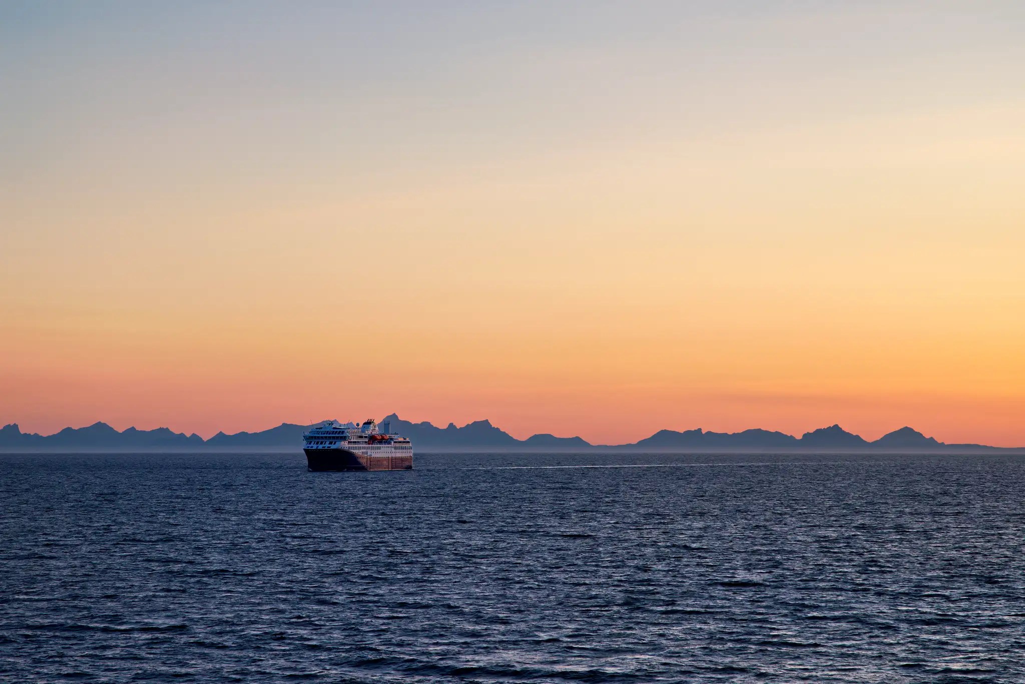 Passagierschiff Hurtigruten auf ruhiger See bei Sonnenuntergang mit Bergsilhouette im Hintergrund