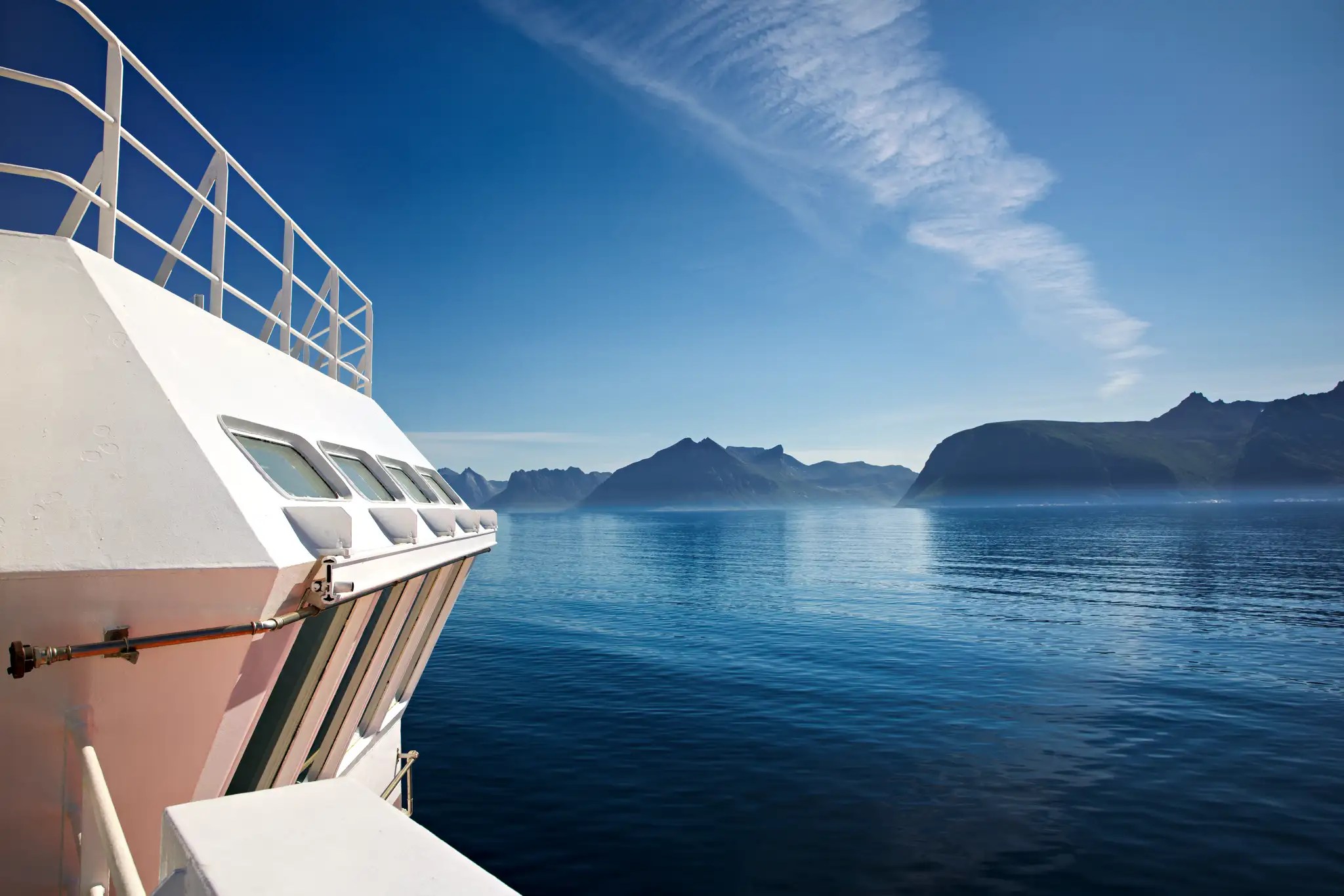 Blick von einem weißen Schiff auf ruhiges Meer und Berge unter blauem Himmel mit Wolken