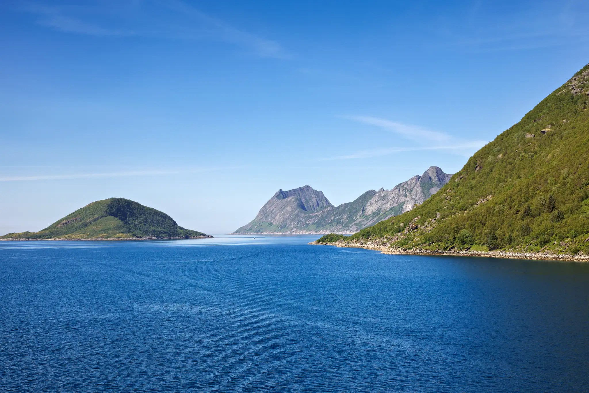 Blick auf ruhiges Meer mit bewaldeten Inseln und Bergen unter klarem blauem Himmel