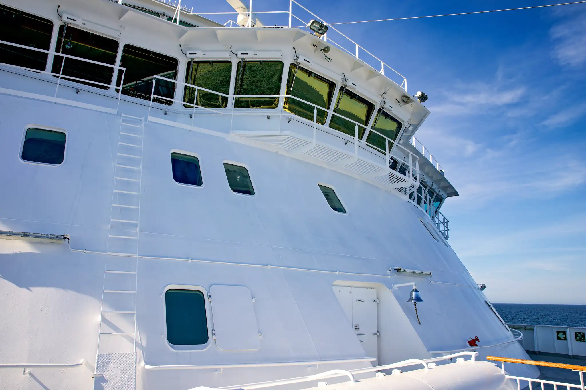 Seitenansicht eines weißen Kreuzfahrtschiffs mit Brücke und Antennen unter blauem Himmel