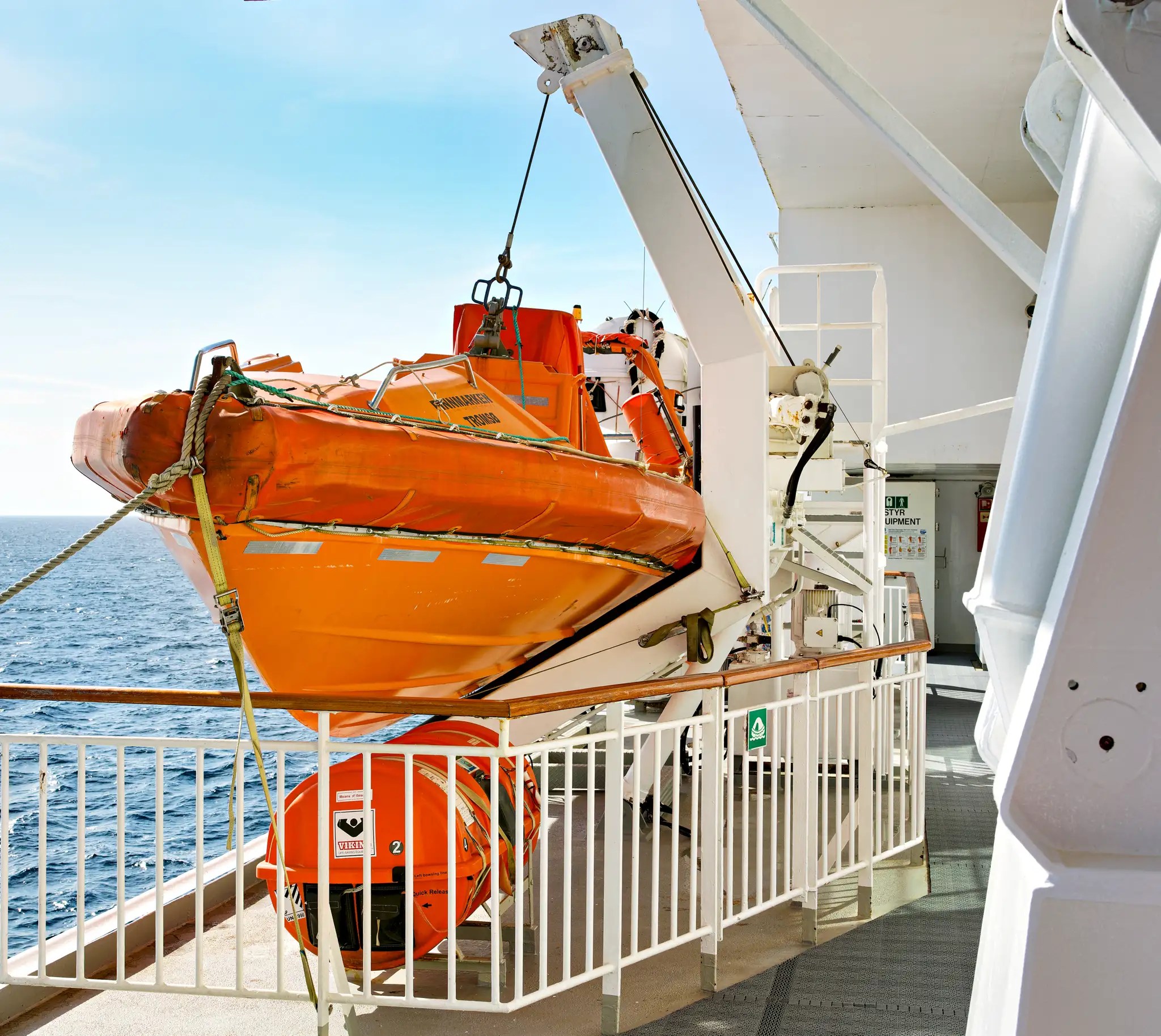 Orangerotes Rettungsboot an einem Ausleger auf dem Außendeck eines Passagierschiffs über dem Meer