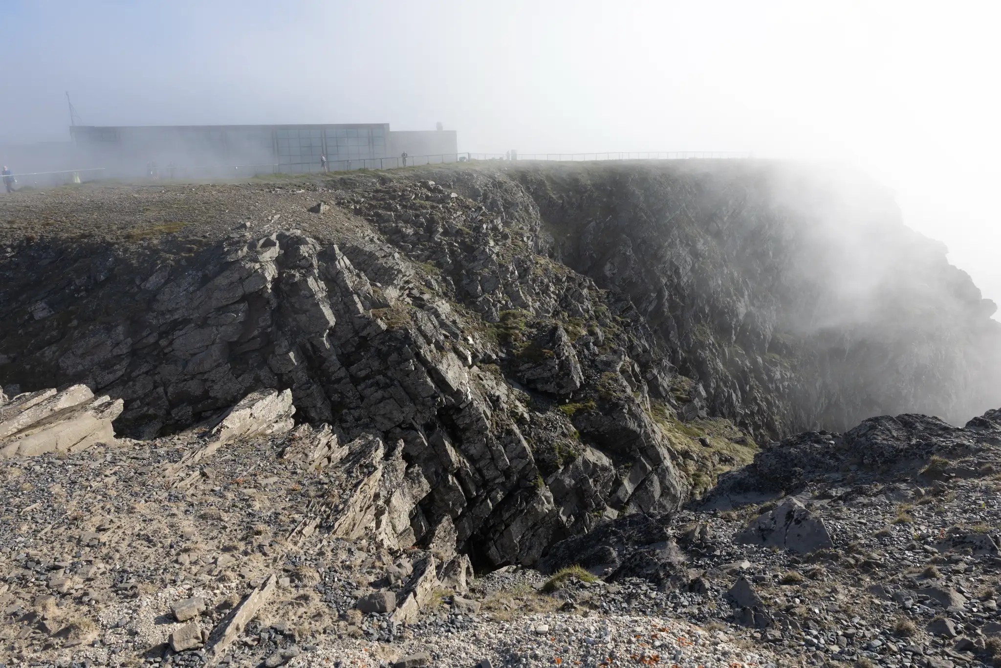 Felsige Klippen am Nordkap mit Nebel und einem Gebäude im Hintergrund