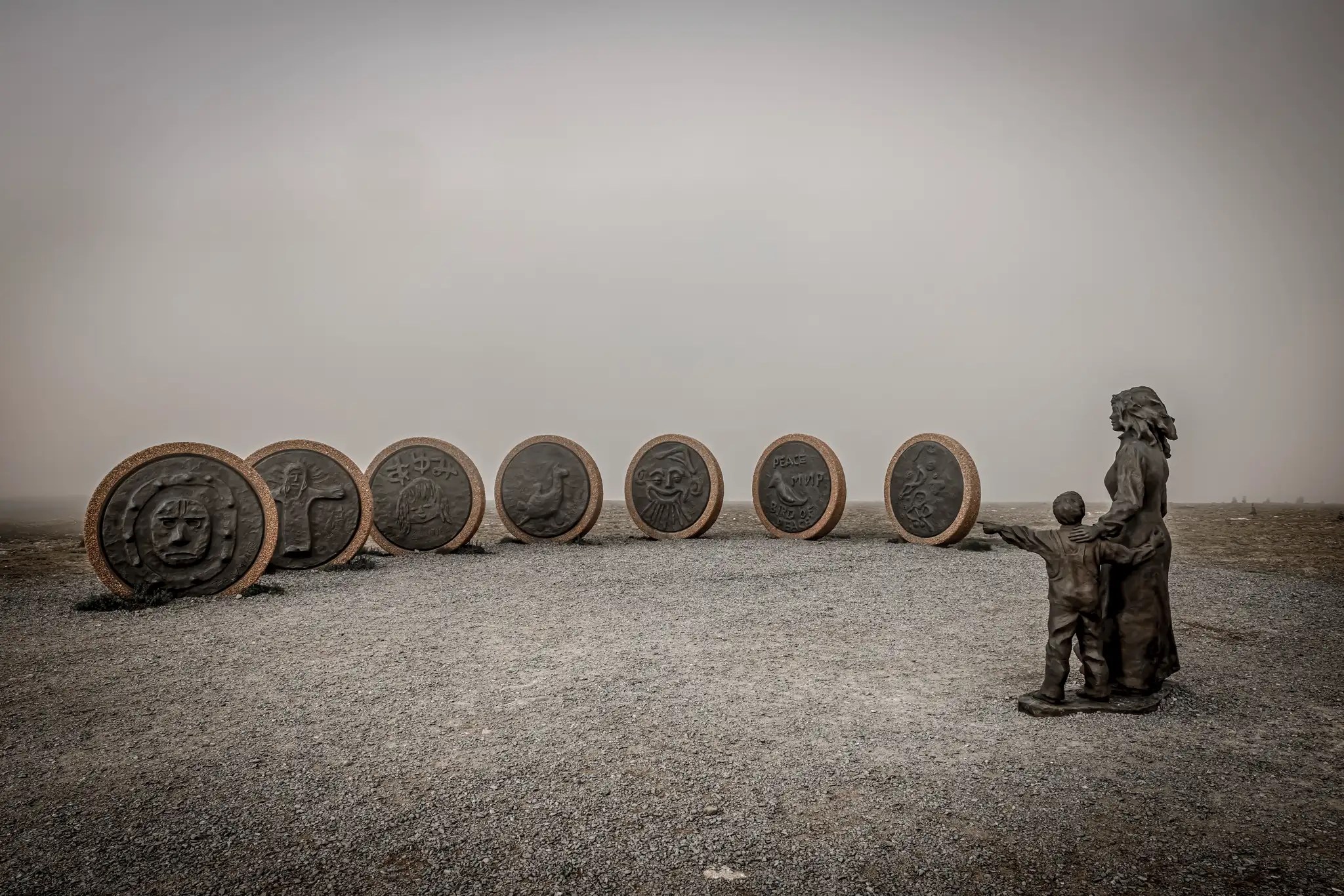 Skulptur am Nordkap mit sieben großen runden Reliefs und zwei Figuren, einer Frau und einem Kind, die auf die Reliefs blicken