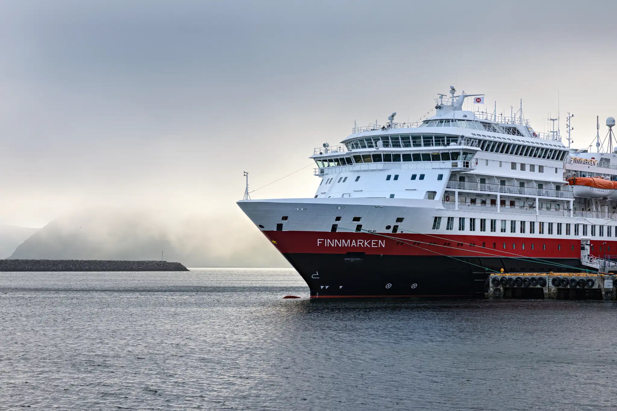 Das Kreuzfahrtschiff 'Finnmarken' der Hurtigruten liegt am Kai in einem ruhigen Hafen bei bewölktem Himmel
