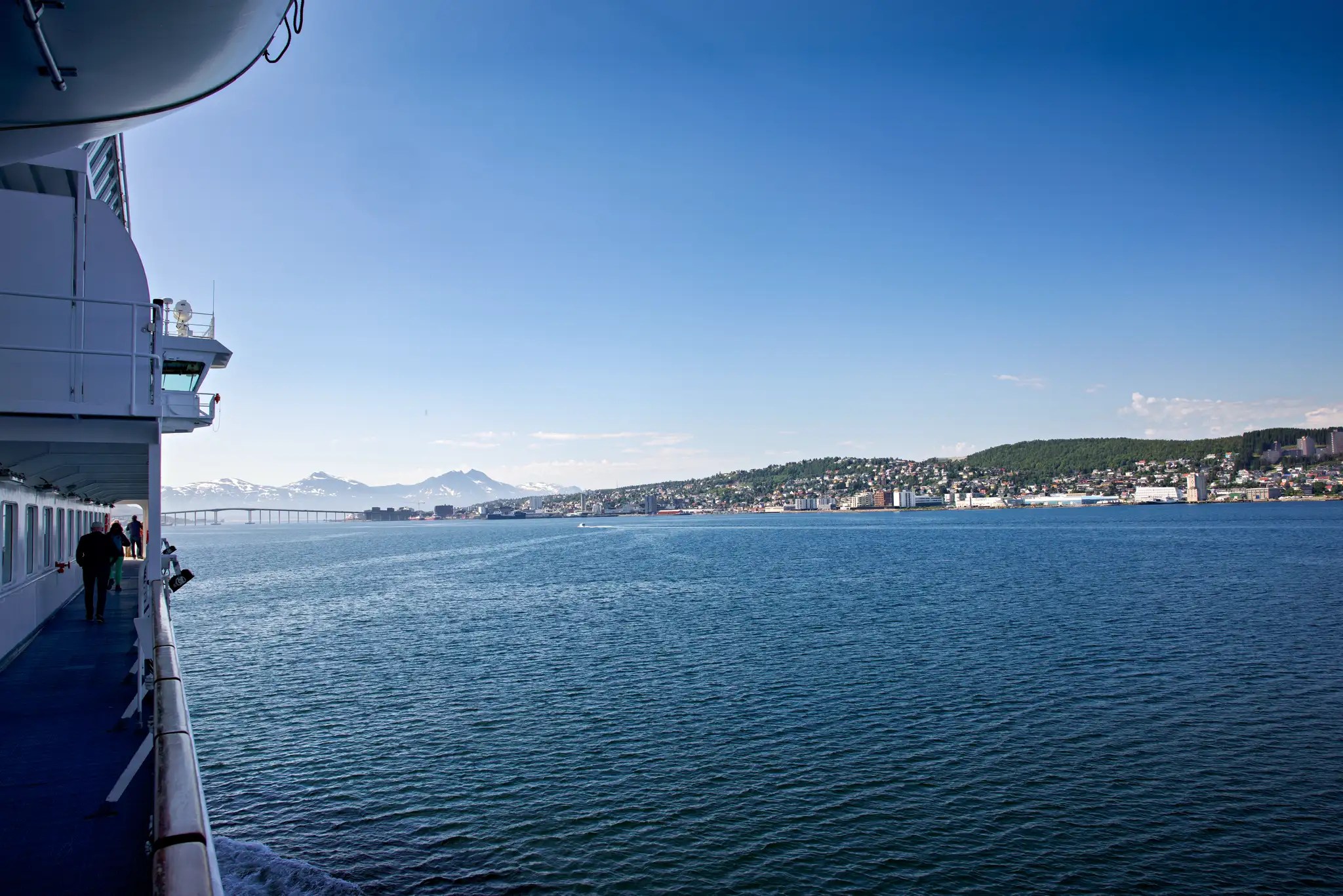 Blick vom Deck eines Schiffes auf ruhiges Meer und Küstenstadt unter klarem Himmel