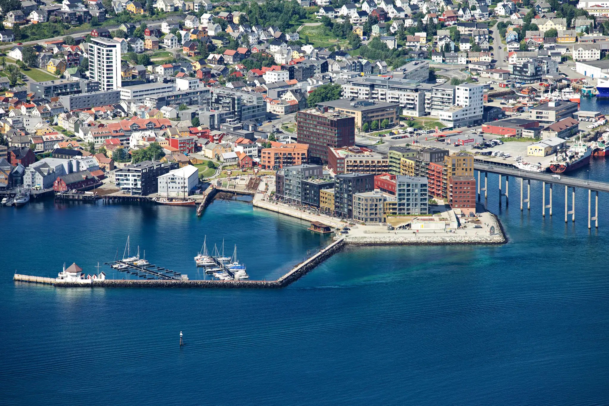 Hafen mit mehreren modernen Gebäuden am Wasser und einem angelegten Hurtigruten-Schiff in einer norwegischen Stadt