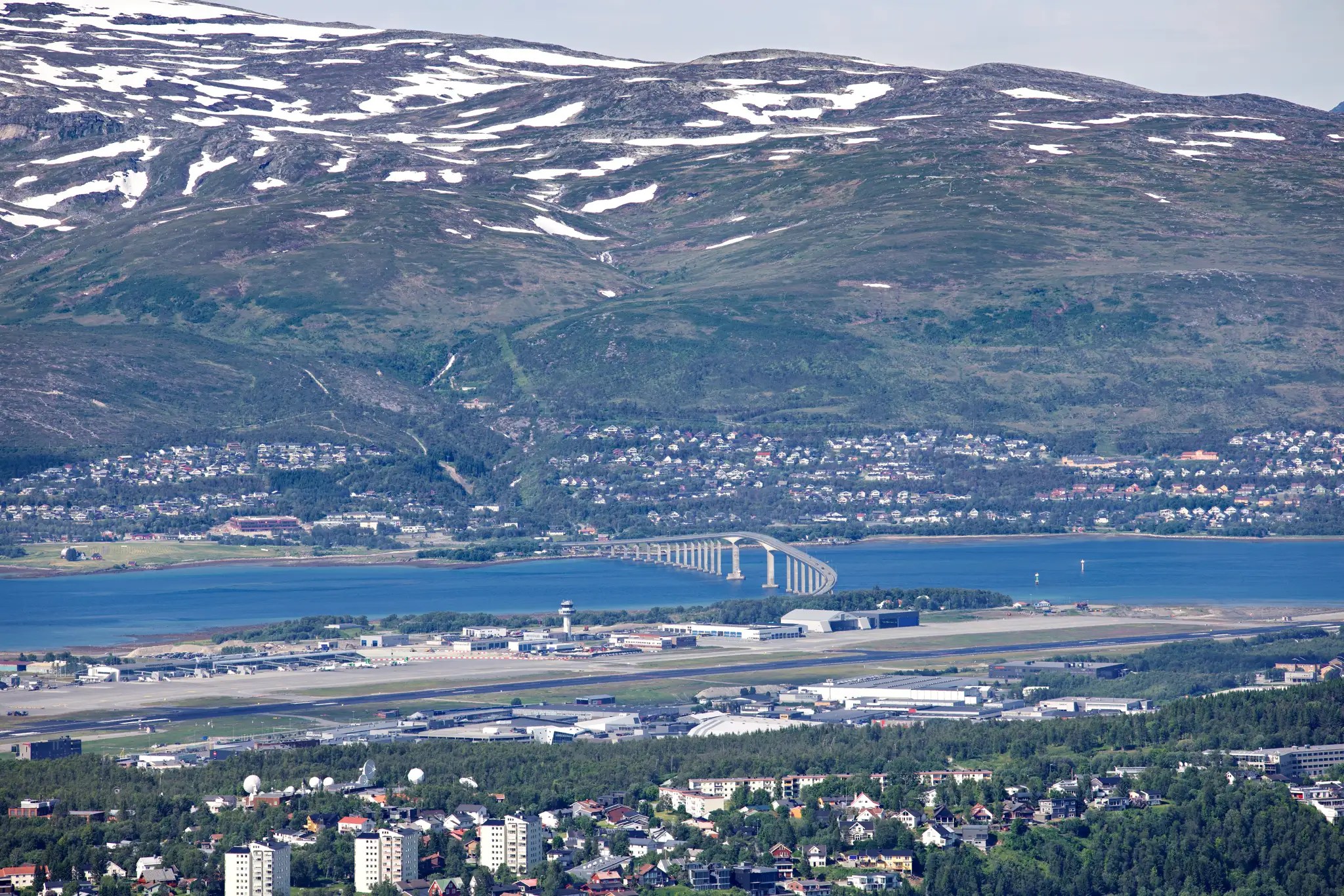 Blick auf die Stadt Tromsø mit der Tromsøbrücke und schneebedeckten Bergen im Hintergrund