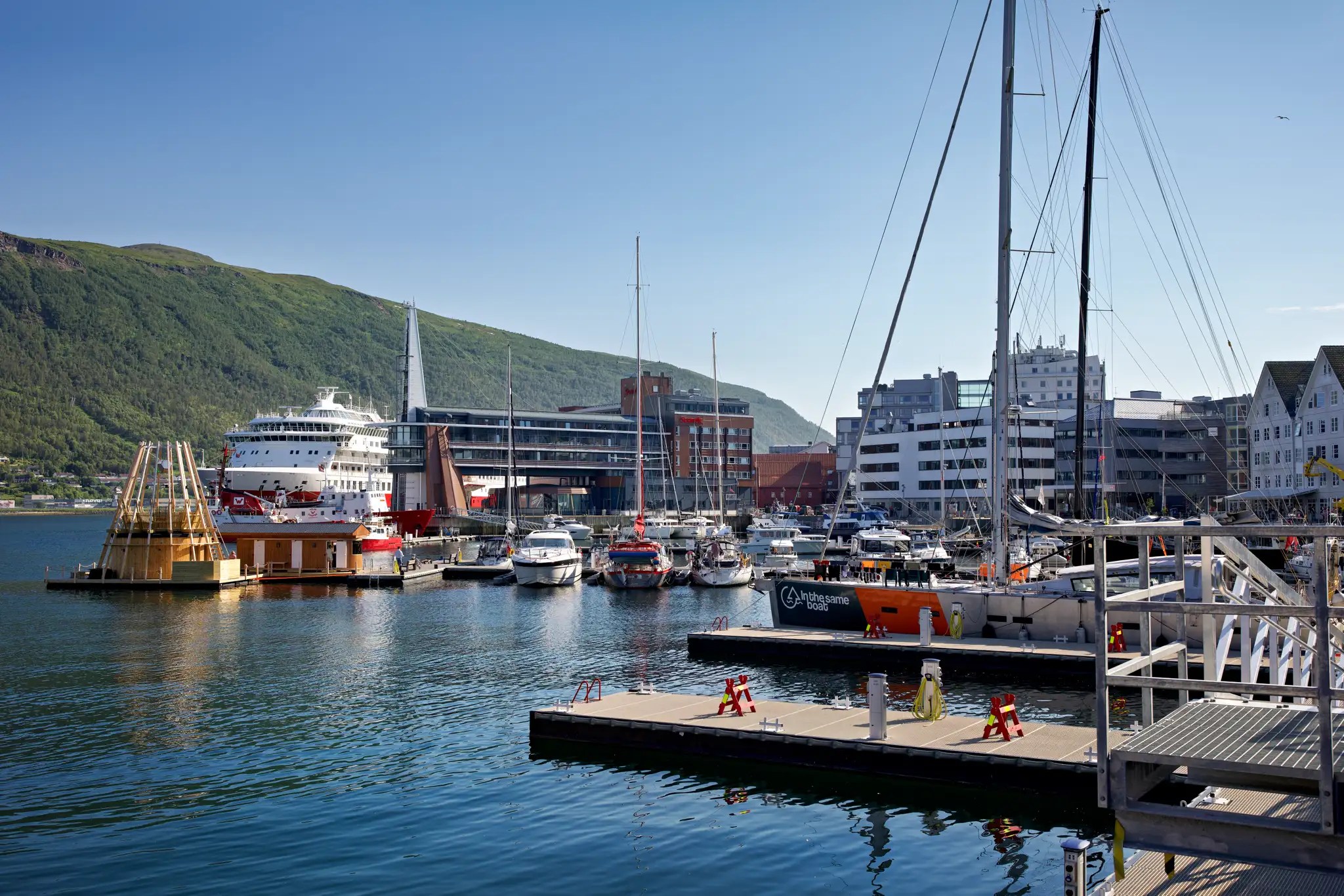 Hafen mit mehreren Booten und Schiffen, im Hintergrund grüne Hügel und moderne Gebäude