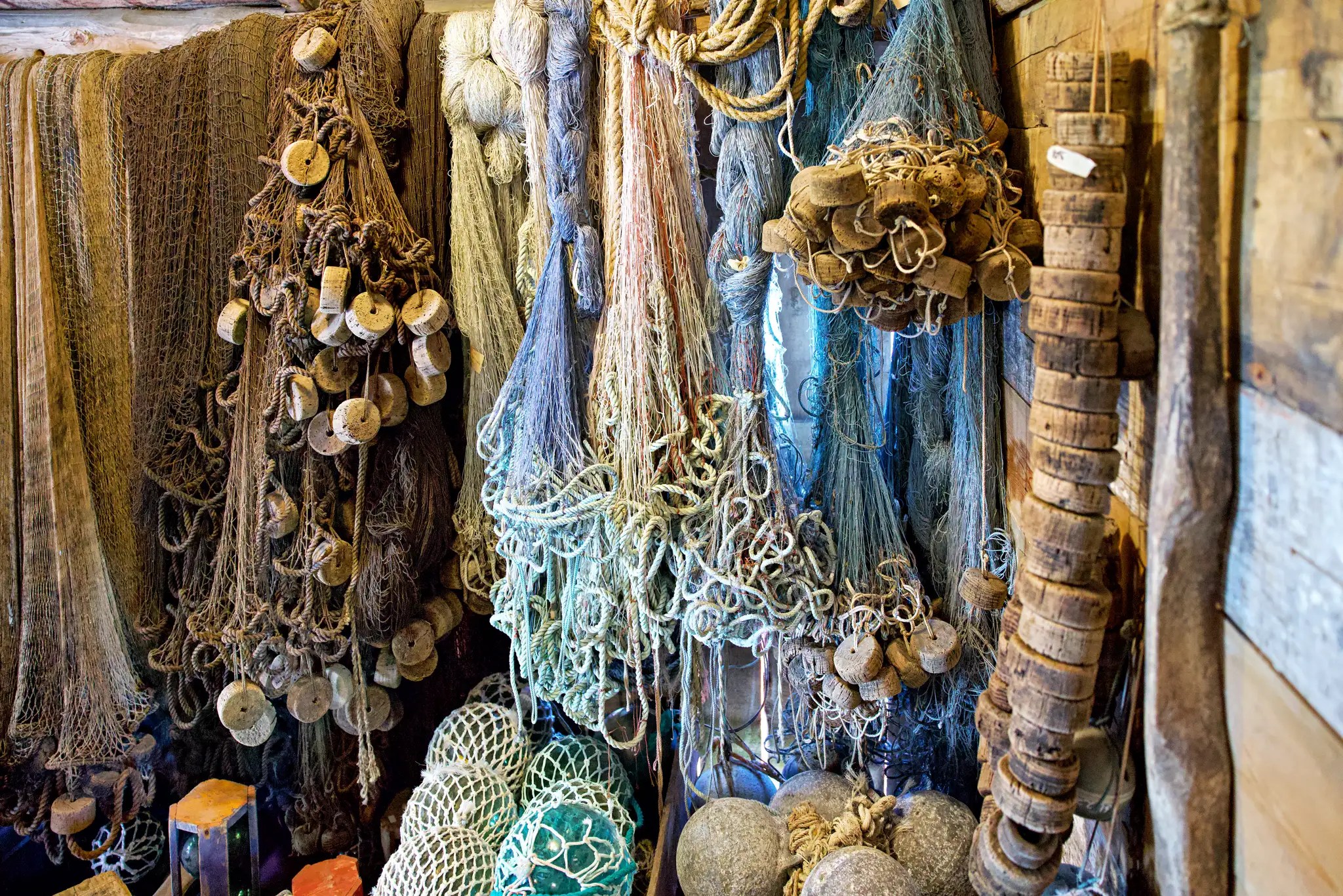 Verschiedene hängende Fischernetze mit Schwimmern und Gewichten in einem Holzraum