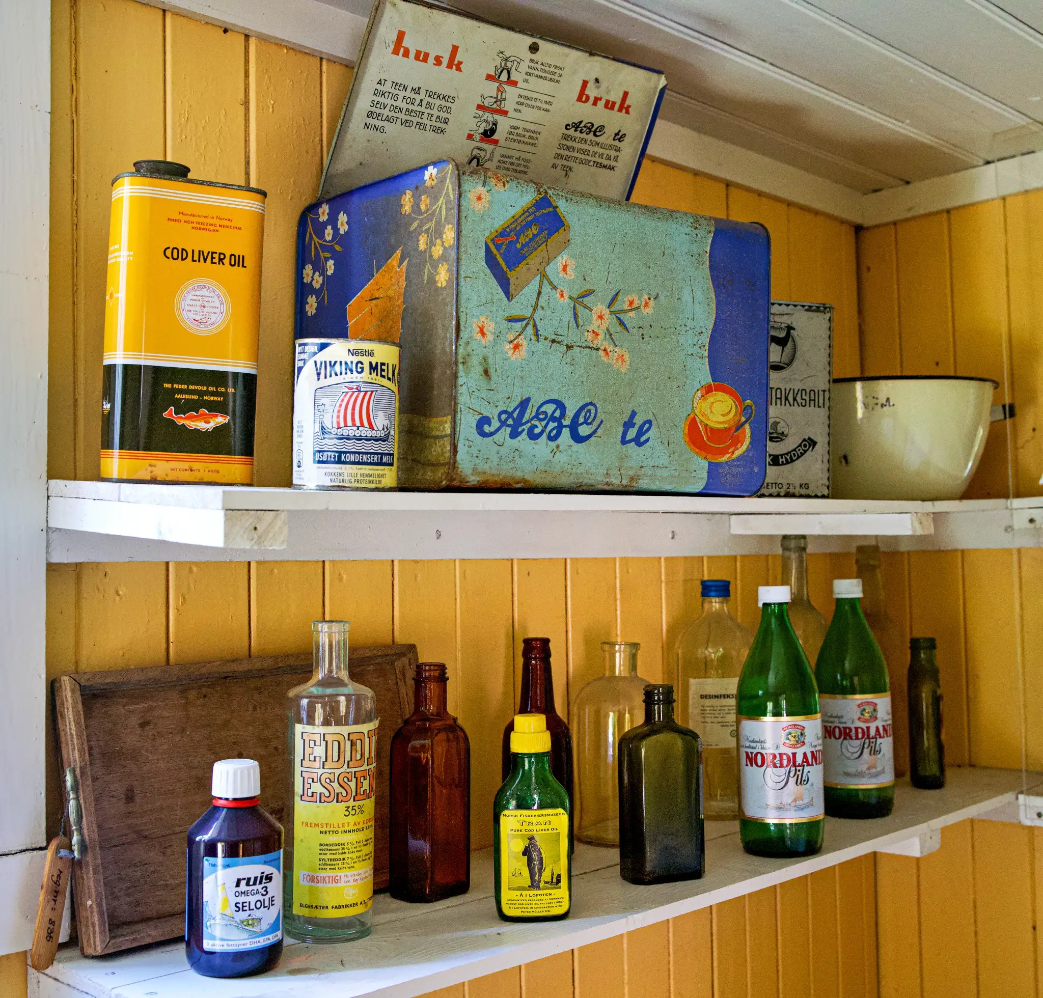 Regal mit verschiedenen alten Flaschen und Dosen, darunter Cod Liver Oil, Viking Melk und Nordland Mineralwasser