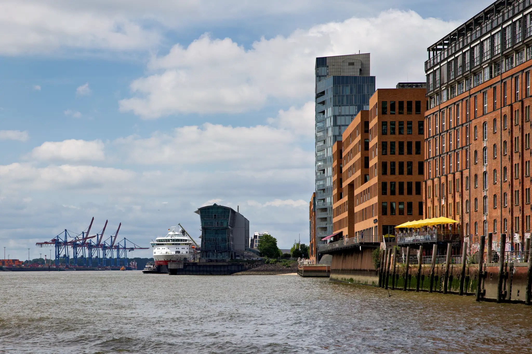 Hafen mit einem weißen Hurtigruten-Schiff am Kai, moderner und historischer Backsteinarchitektur am Ufer, Kräne im Hintergrund