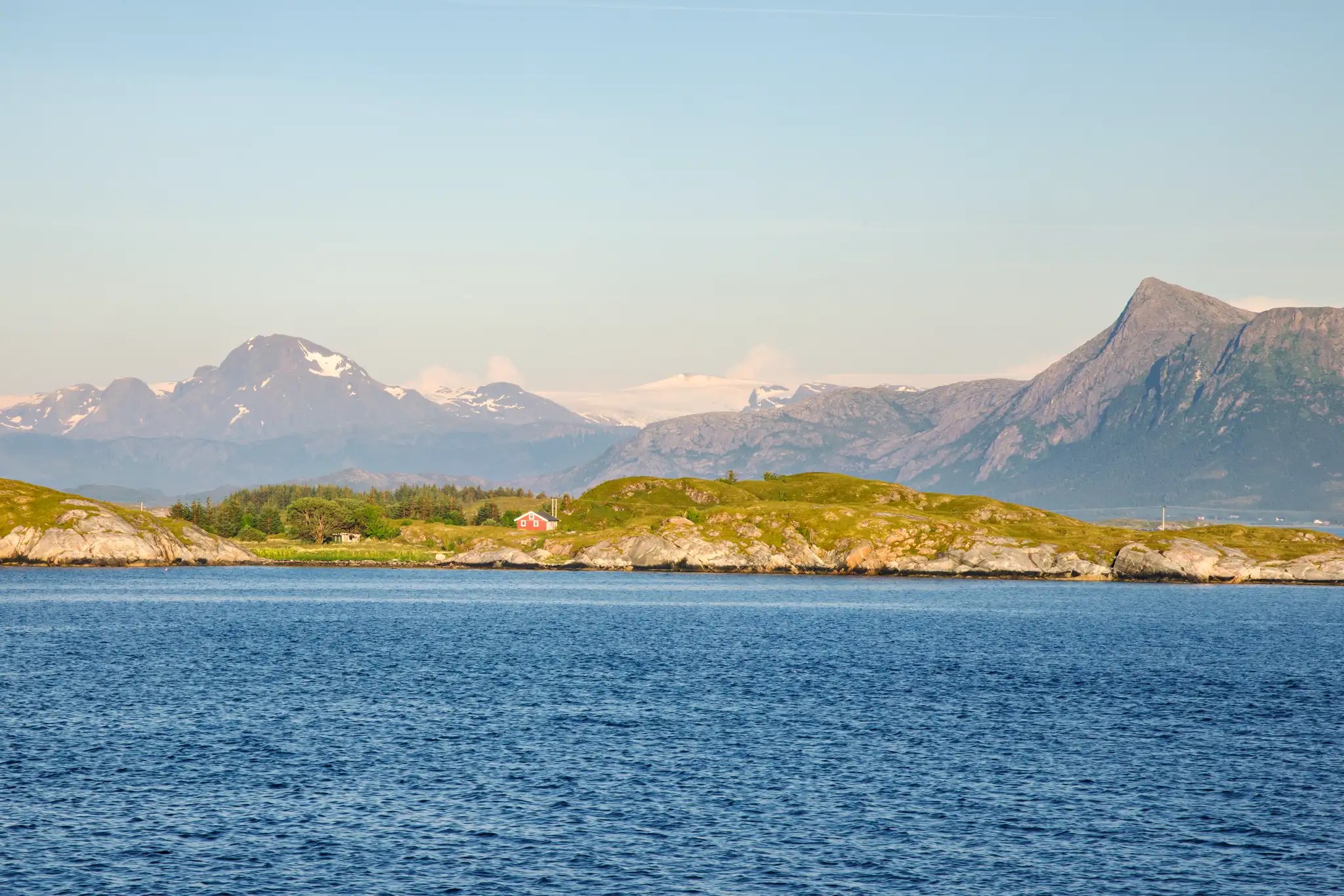 Blick auf eine norwegische Küstenlandschaft mit Bergen im Hintergrund und ruhigem Meer im Vordergrund