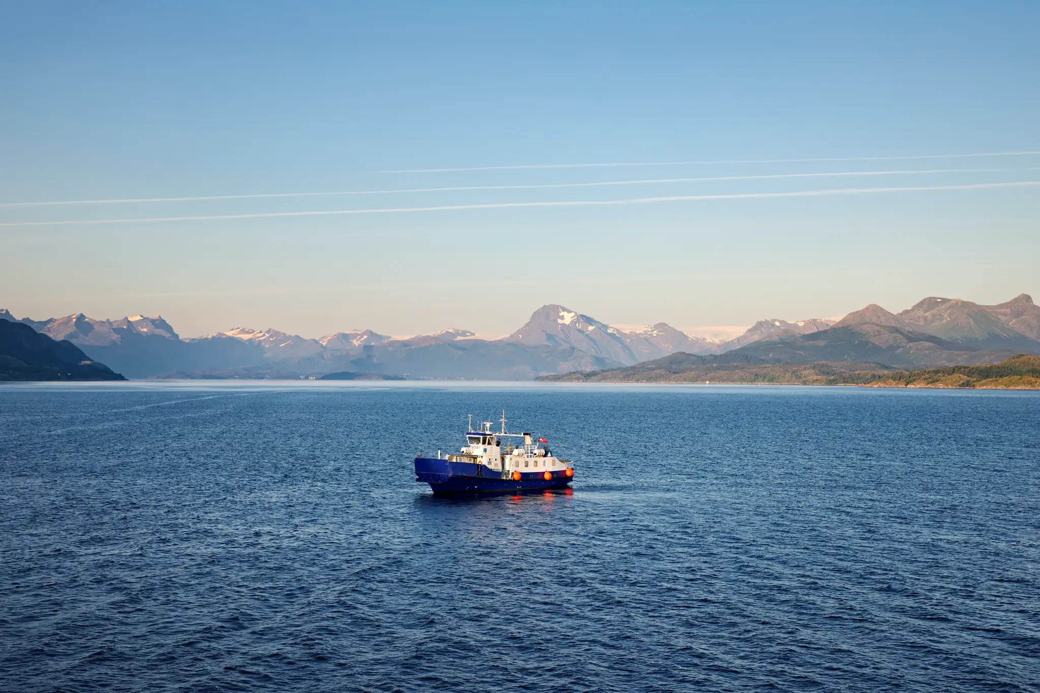 Kleine Fähre auf ruhigem Meer vor Bergkulisse mit klarem Himmel