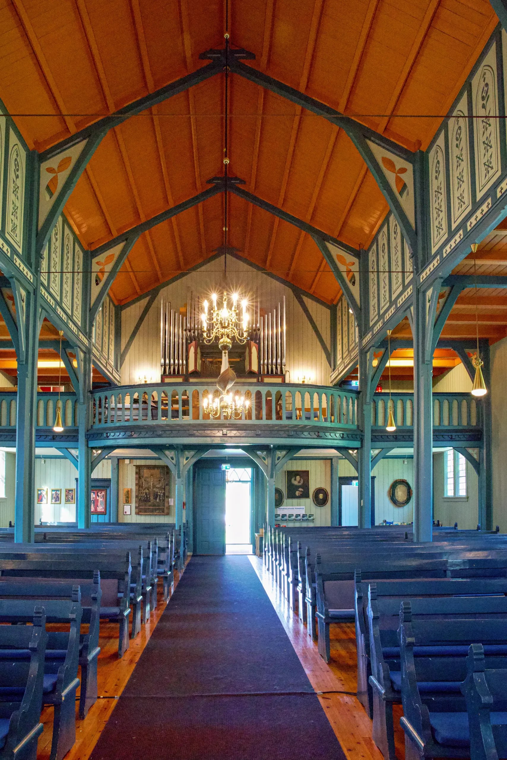 Innenraum einer Kirche mit hölzernen blauen Bänken, rotem Teppich und Orgel über dem Eingang