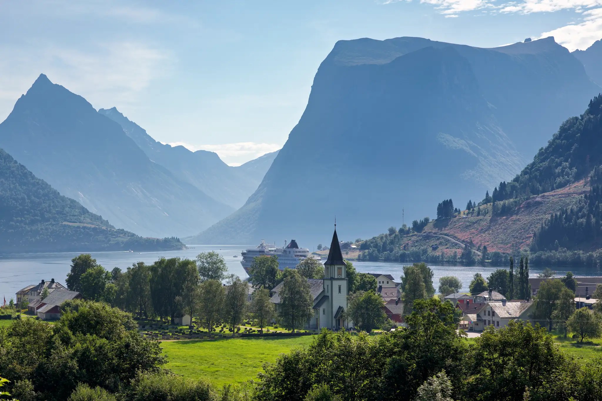 Fjordlandschaft mit Bergen, Kirche und Hurtigruten-Kreuzfahrtschiff im Wasser