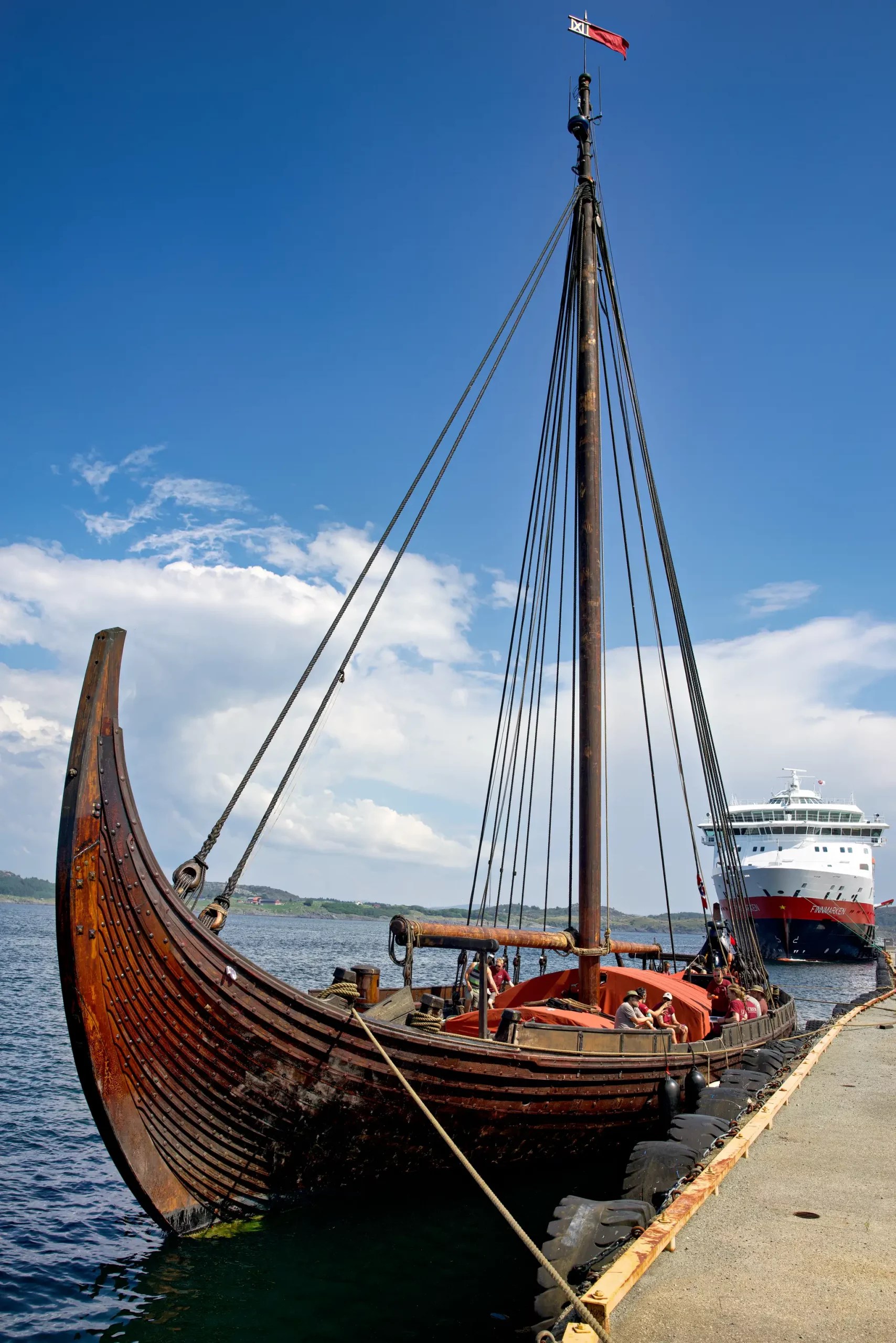 Traditionelles Wikingerschiff mit Mast und Flagge am Kai, im Hintergrund modernes Kreuzfahrtschiff