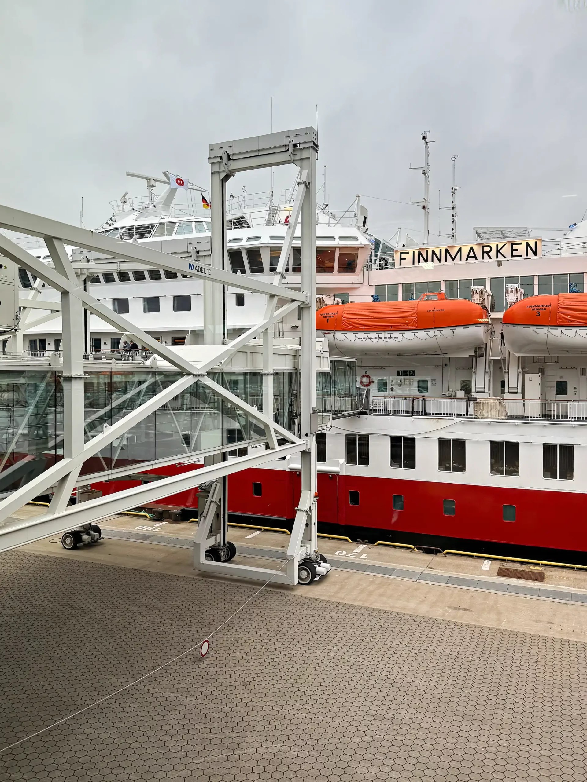 Passagierschiff 'Finnmarken' der Hurtigruten mit Rettungsbooten am Hafen unter bewölktem Himmel. Eine Gangway führt zum Schiff