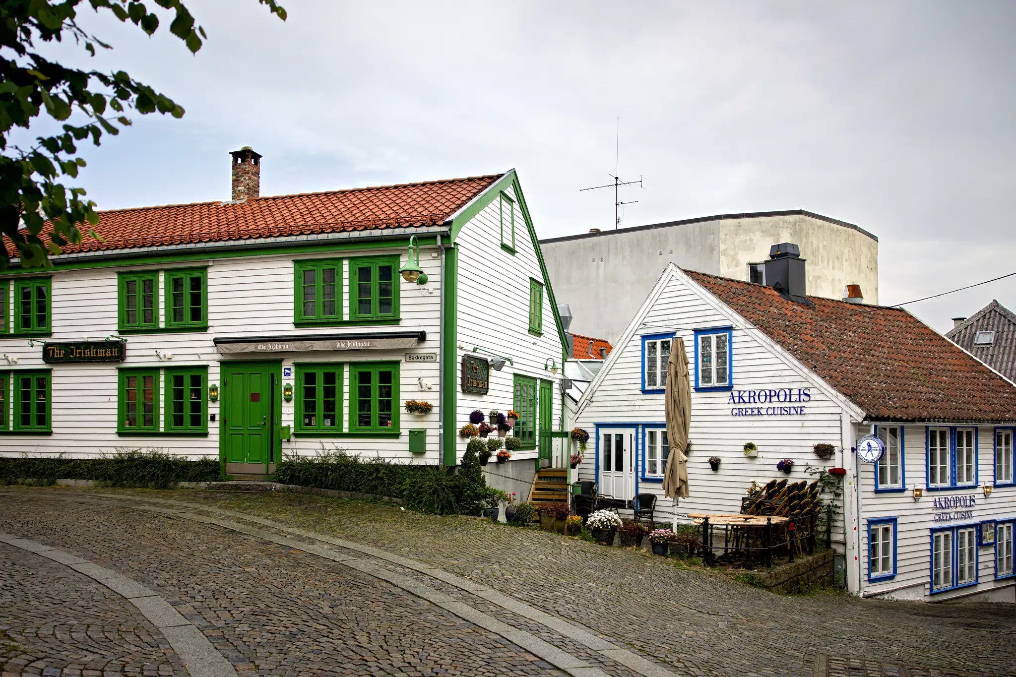 Traditionelle weiße Holzhäuser mit grünen und blauen Fensterrahmen an einer gepflasterten Straße in Norwegen