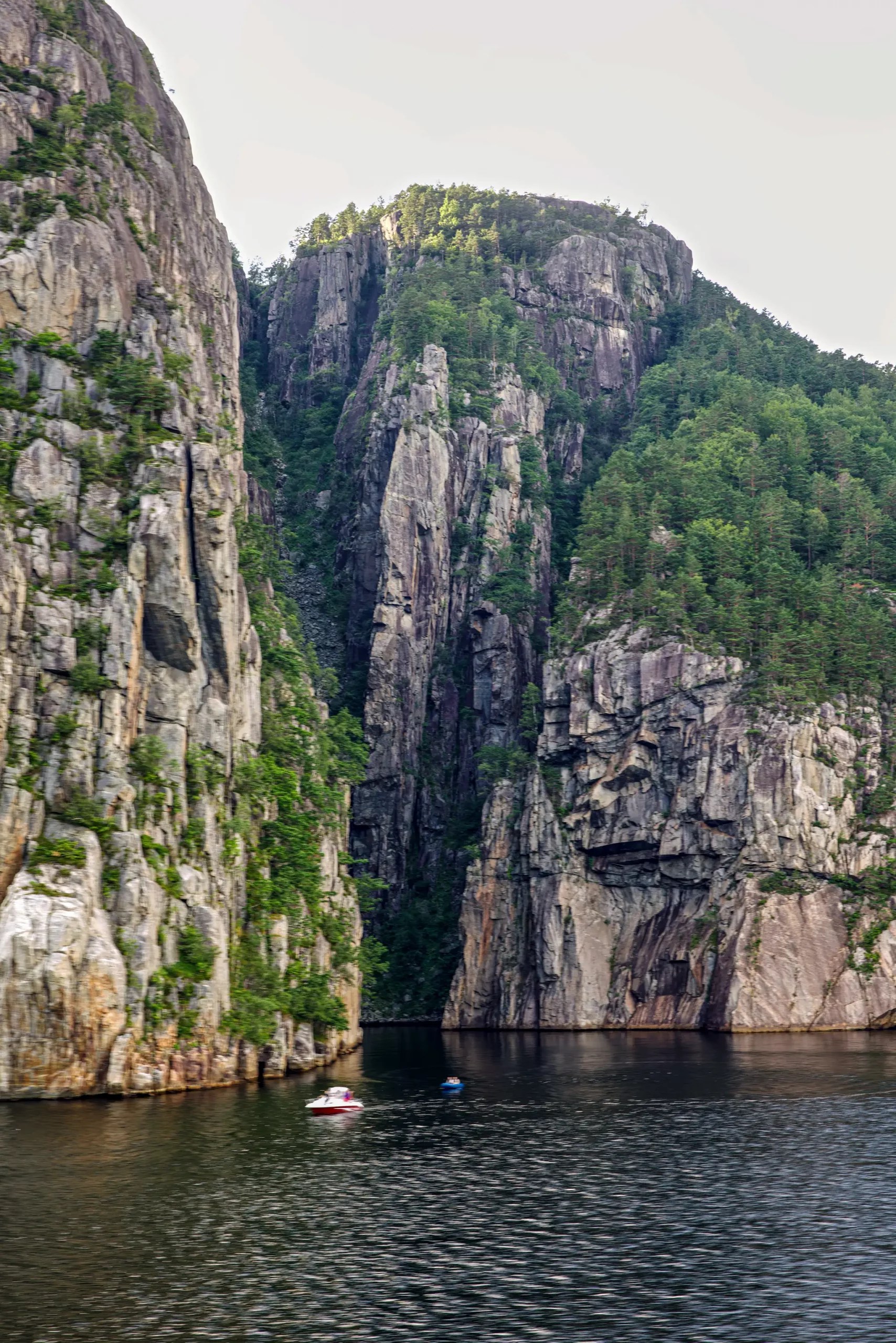 Schmale Wasserstraße zwischen hohen, bewaldeten Felsklippen mit zwei kleinen Booten auf dem Wasser
