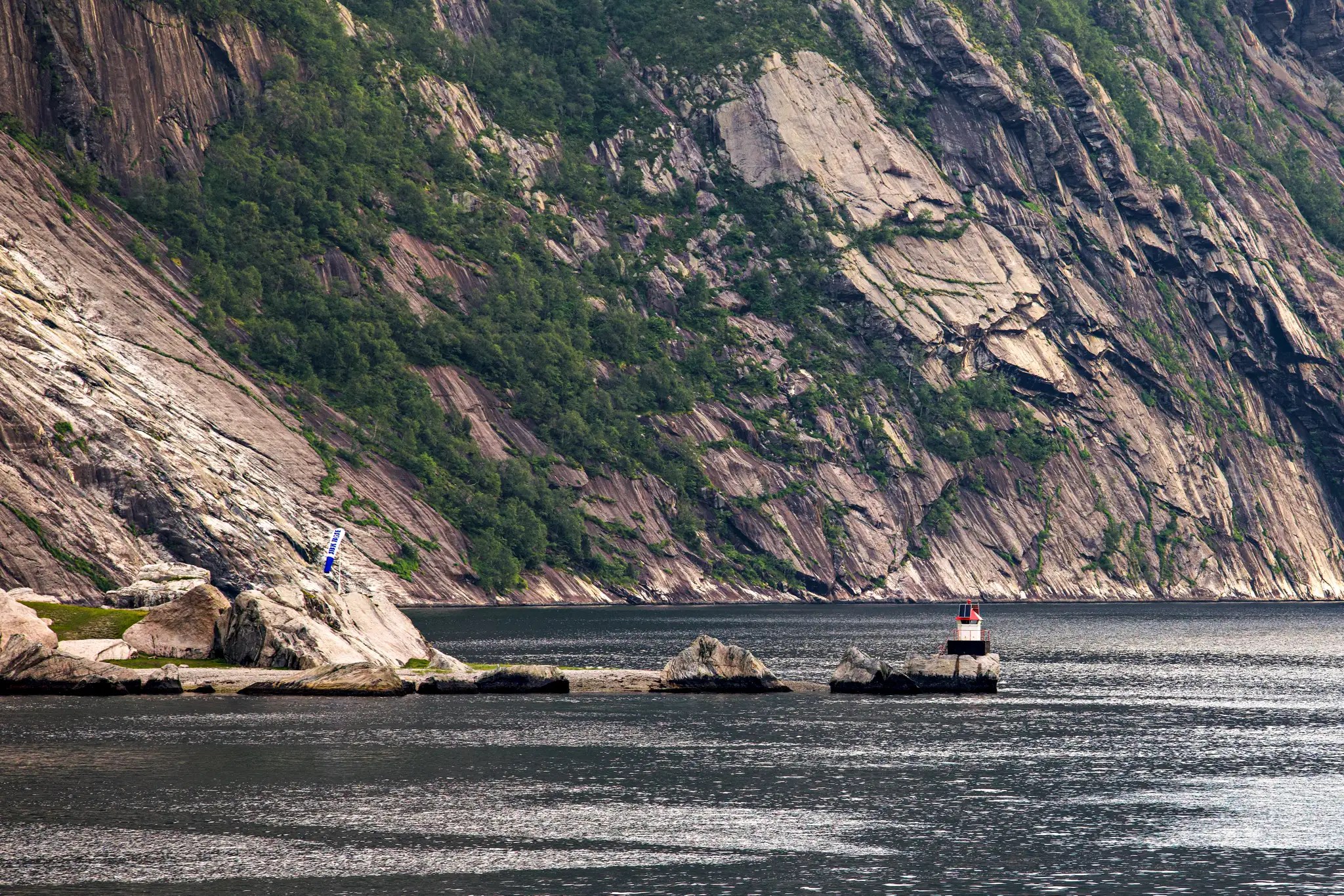 Felsige Küste mit steilen Klippen und einem kleinen Leuchtturm am Wasser in Norwegen