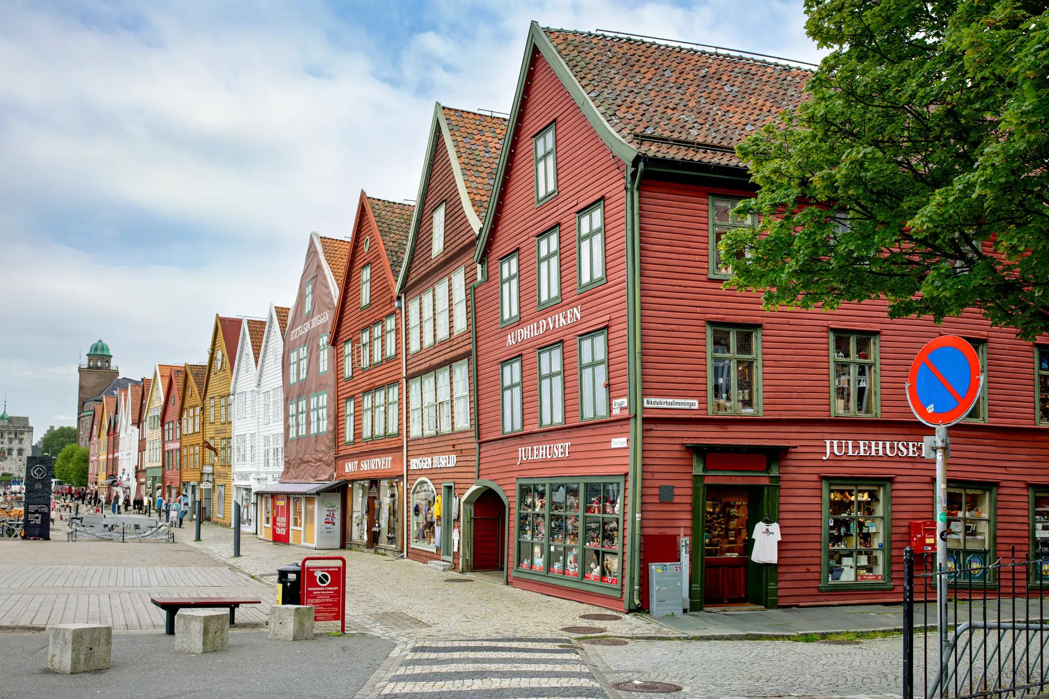 Reihe historischer Holzhäuser mit spitzen Giebeln in Bryggen, Bergen, Norwegen, mit Geschäften und Fußgängern
