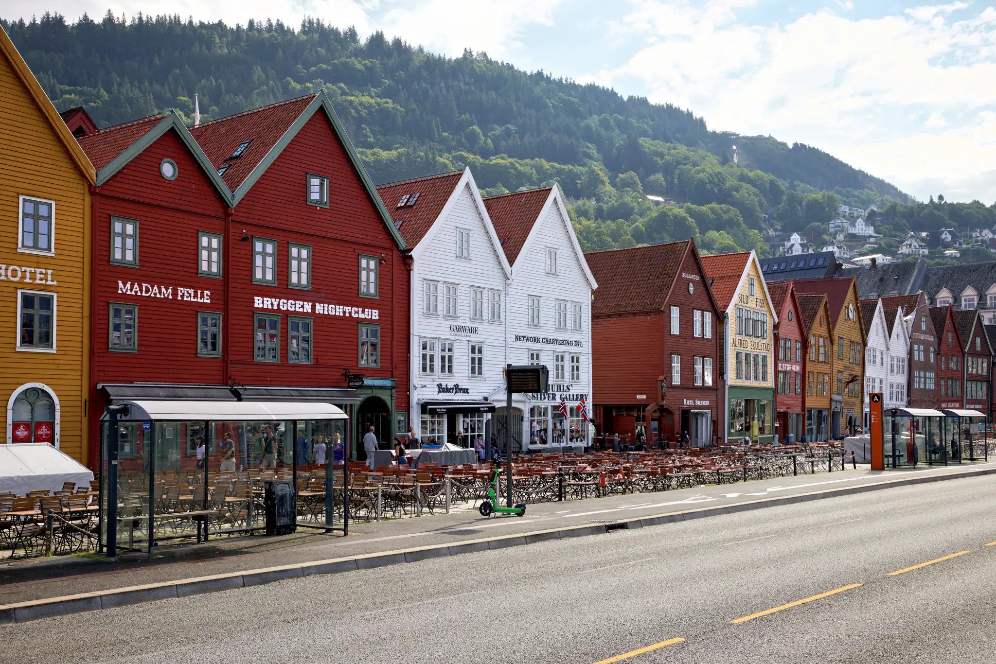 Reihe bunter Holzhäuser am Hafen von Bergen, Norwegen, vor bewaldeten Hügeln