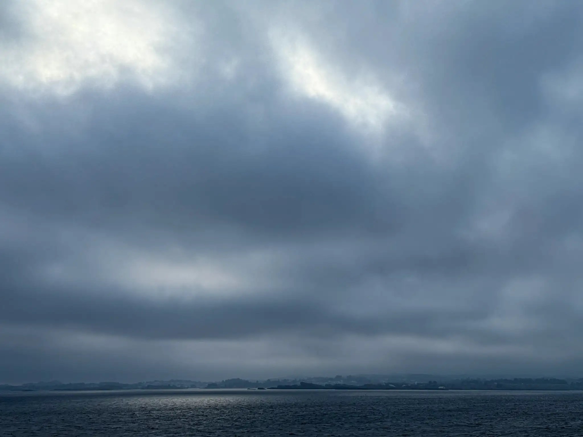 Dunkle Wolken am Himmel über einer ruhigen Wasserfläche mit entfernten Hügeln