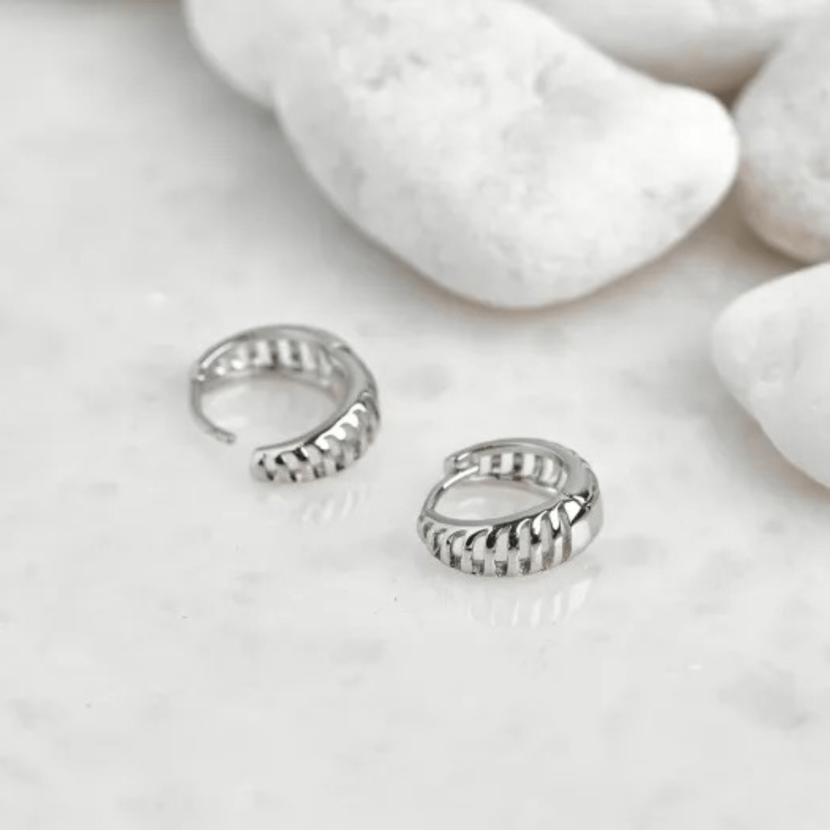 A pair of larger-sized silver-tone huggie earrings featuring a prominent, sculptural ribbed design with deep, organic grooves