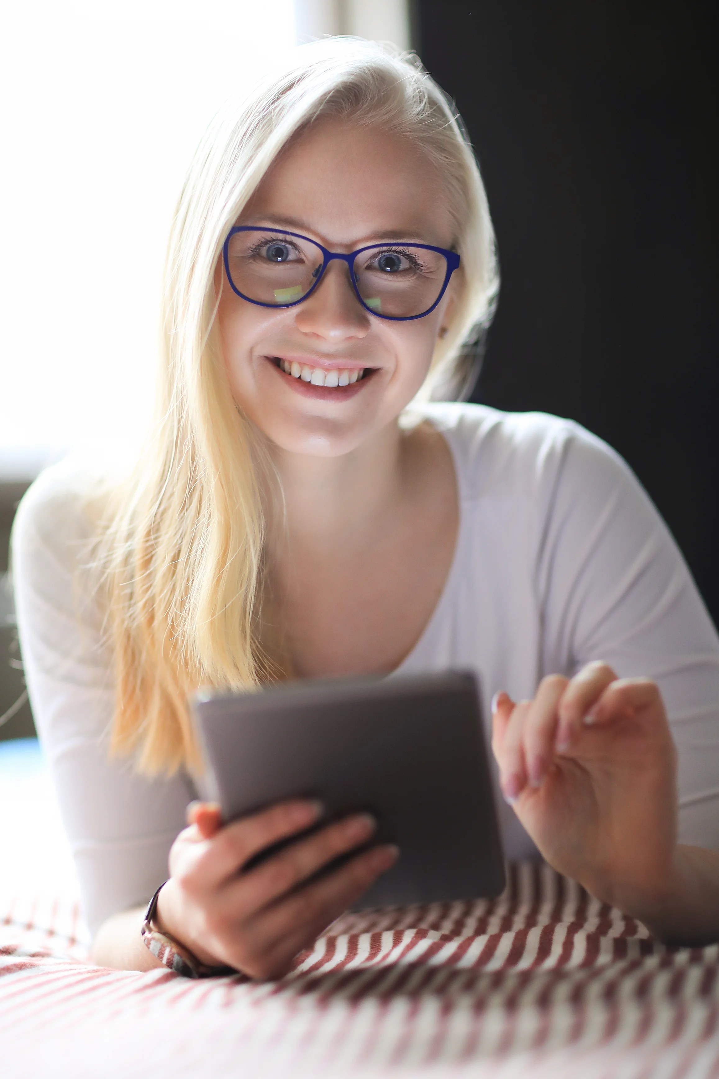 lovely blonde woman with eyeglasses posing while using a tablet