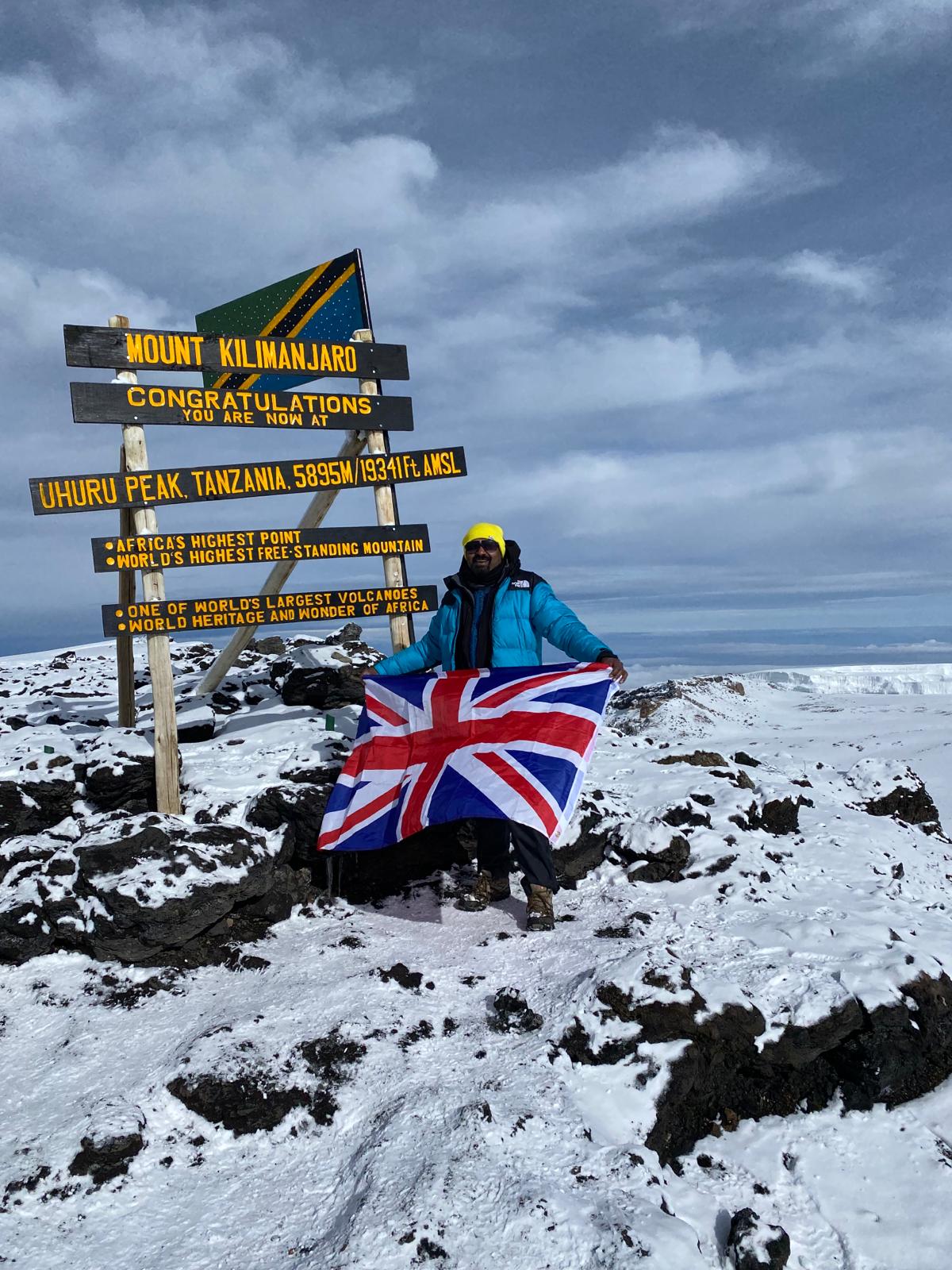 A man holding British flag on the peak of Mount Kilimanjaro