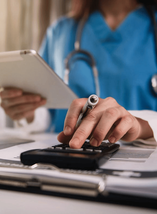 Healthcare professional in scrubs using a tablet and calculator to manage medical billing paperwork