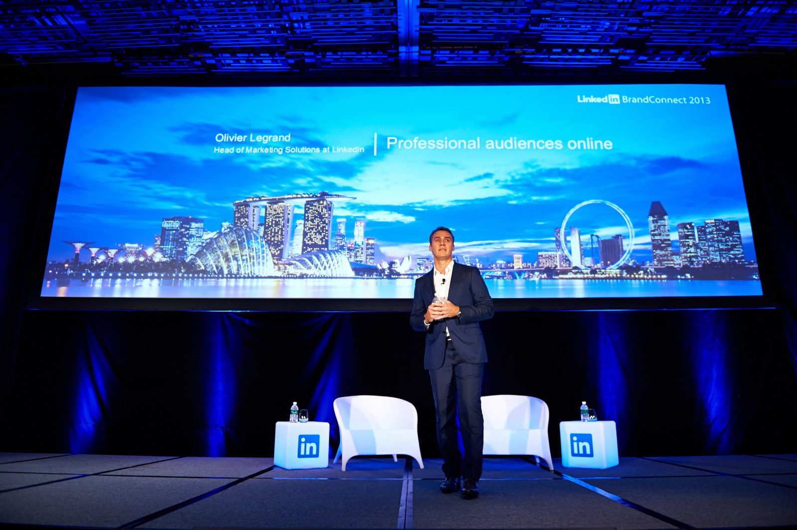 A group of diverse professionals in business attire are engaged in a meeting around a conference table in a modern office setting. The room features large windows allowing natural light to illuminate the space. Some team members are actively discussing, while others are attentively listening and taking notes. Laptops, documents, and coffee cups are visible on the table, indicating a productive work environment. The overall atmosphere is collaborative and focused, reflecting a corporate culture of teamwork and communication.